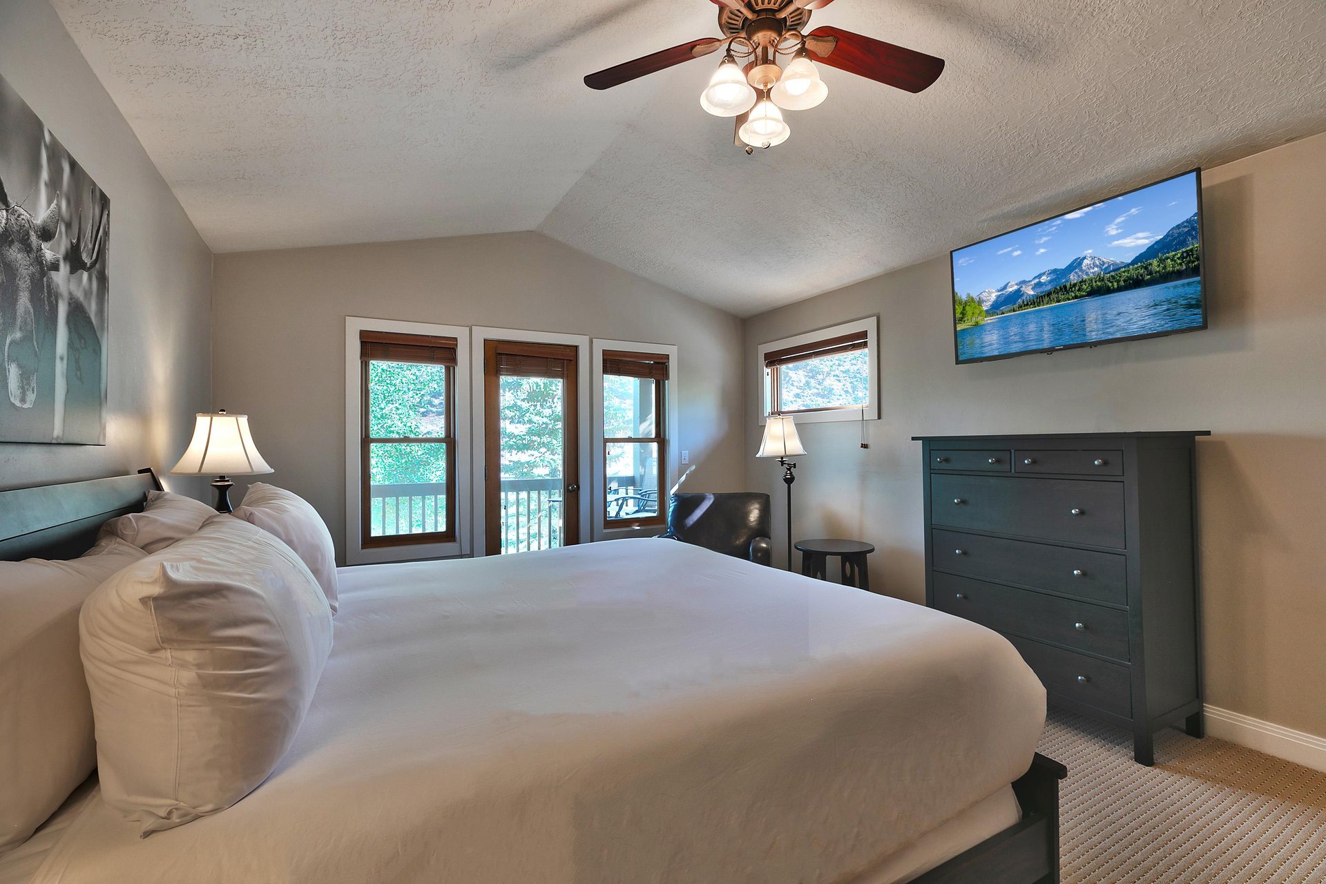 Main bedroom suite with wall mounted flat screen TV, dark wood dresser and black leather accent chair