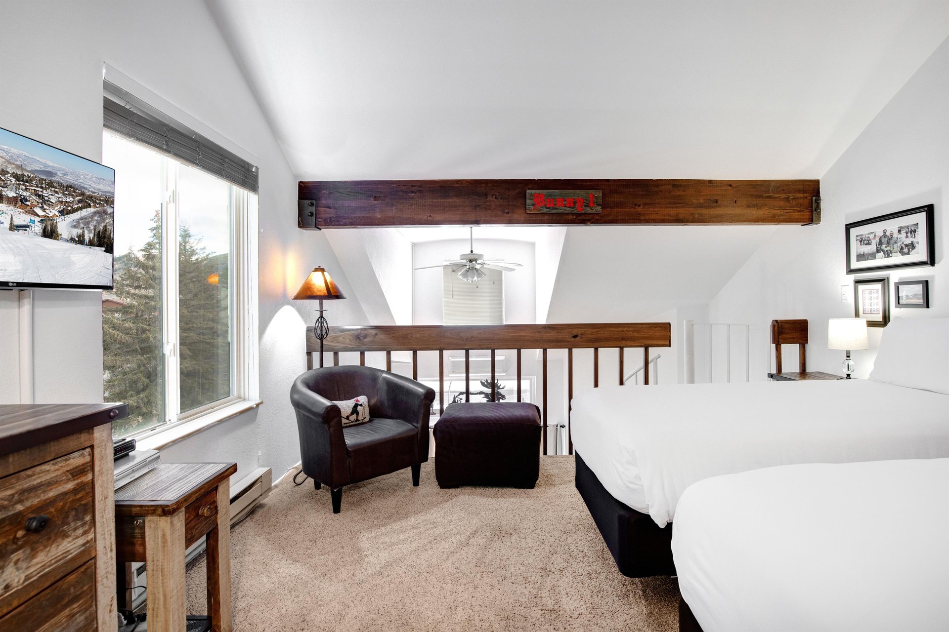 Unwind in your spacious bedroom featuring exposed wooden beams, comfortable seating area, and peaceful mountain views through the large windows.