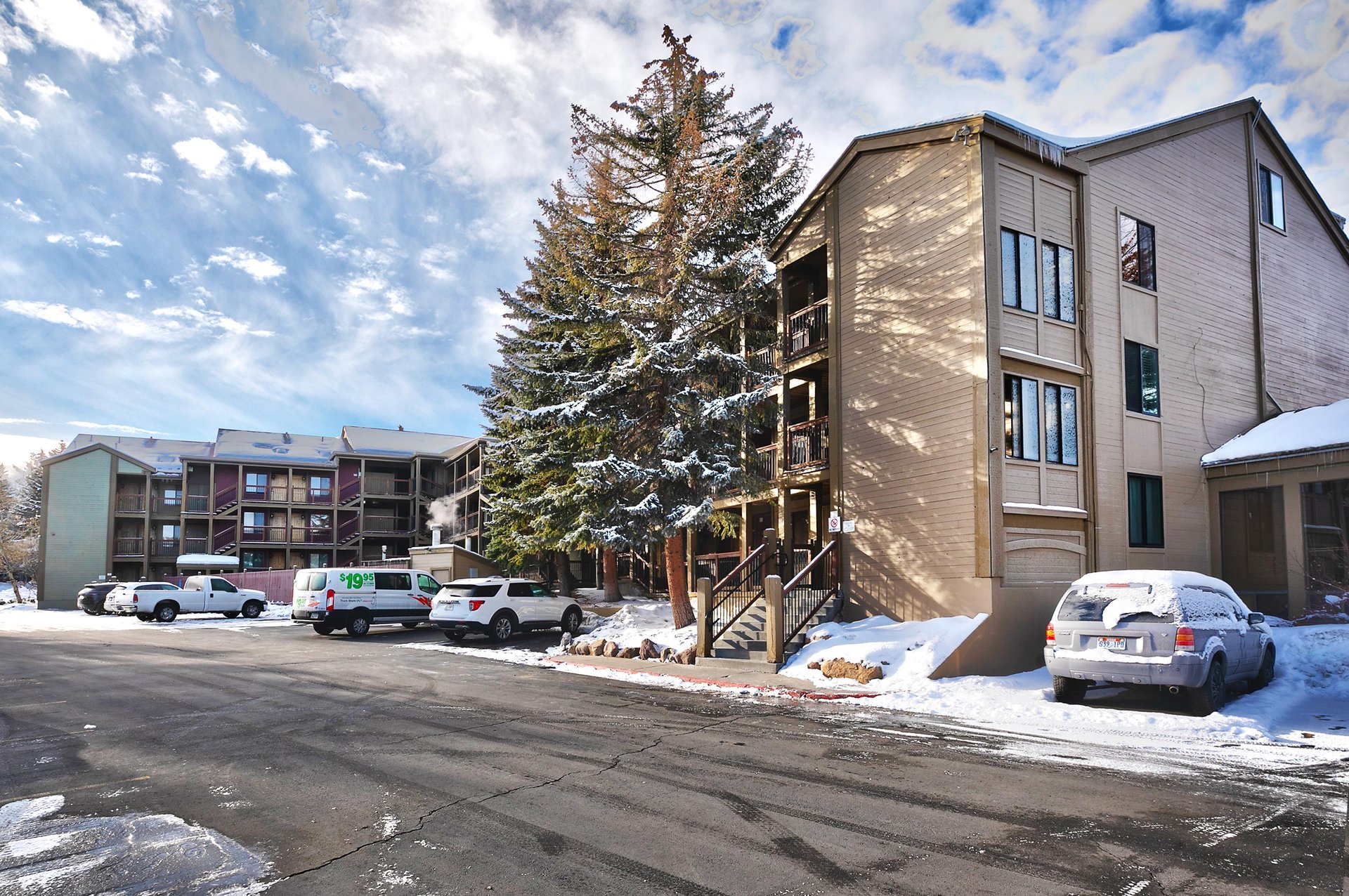 Winter exterior view of the property buildings with snowcovered evergreen trees and convenient parking available for guests.