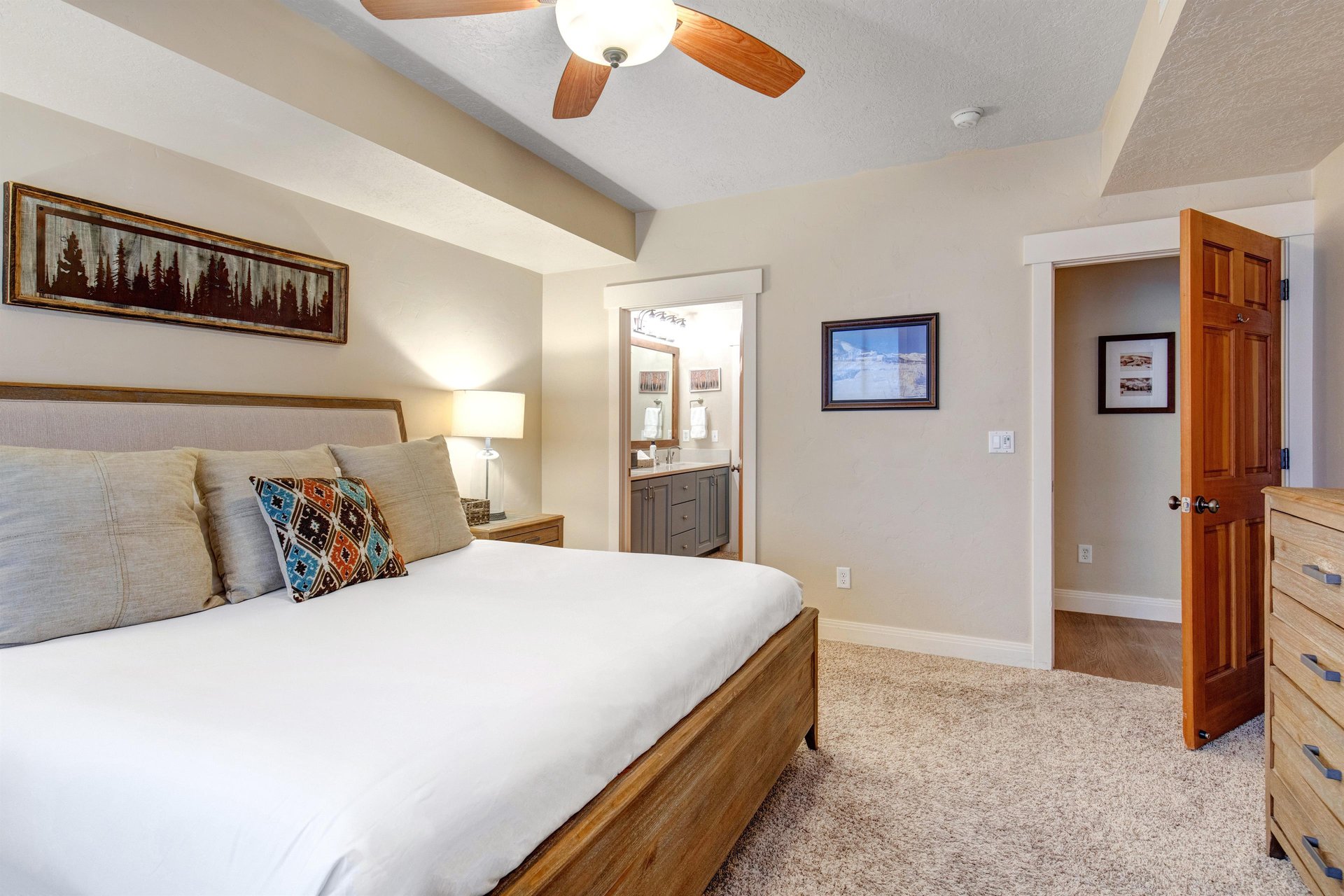 Sink into plush bedding and unwind beneath the ceiling fans gentle breeze. Your private ensuite bathroom awaits through the doorway, while artwork and warm wood tones create a cozy mountain retreat.