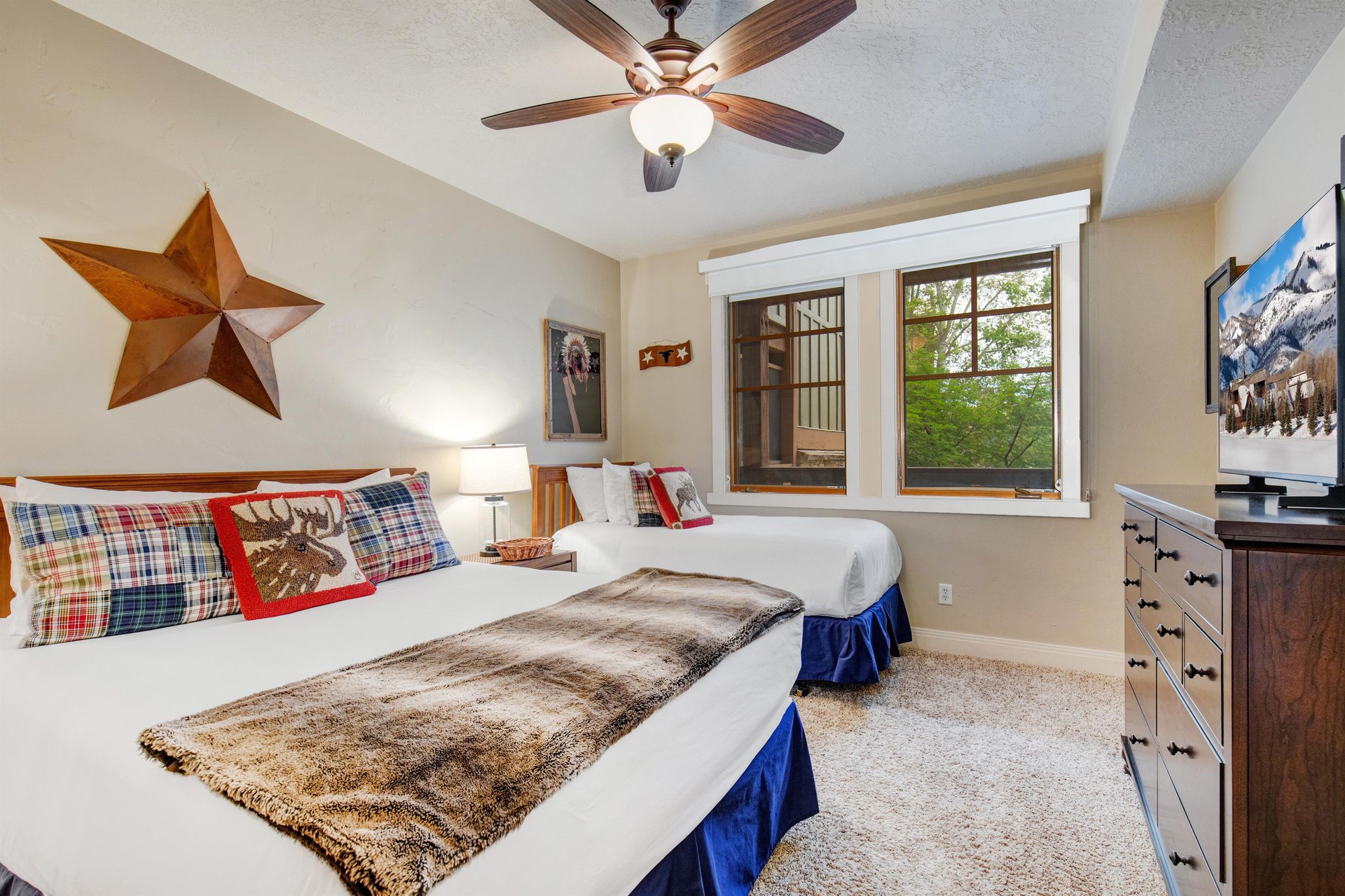 Unwind in this cozy bedroom with plush beds dressed in soft linens, warm rustic décor, and natural light streaming through windows that frame leafy views—your perfect retreat after a day of adventure.