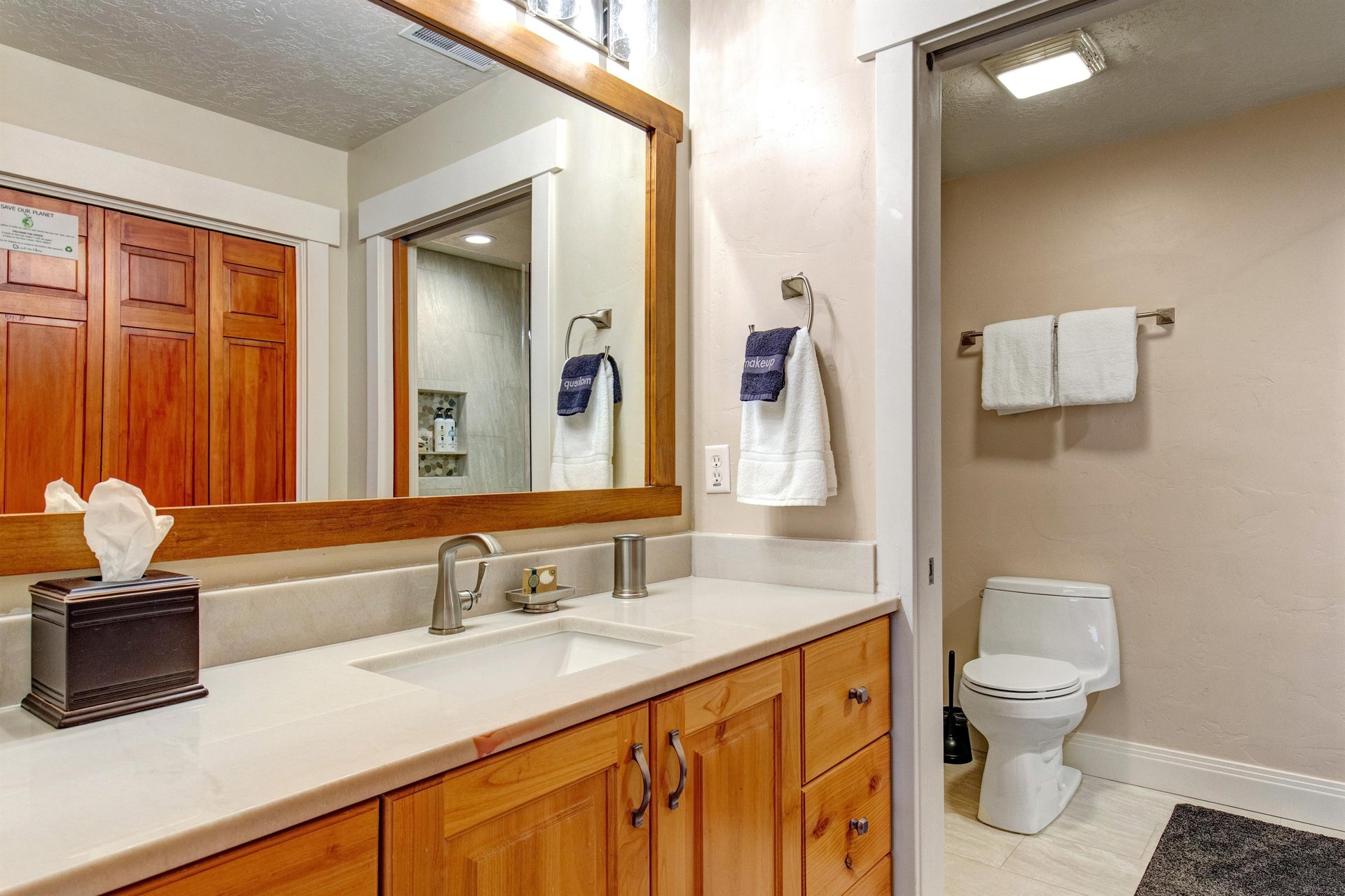 Fresh linens await in this bright bathroom with warm wood tones, a spacious vanity, and modern fixtures—all ready for your arrival.