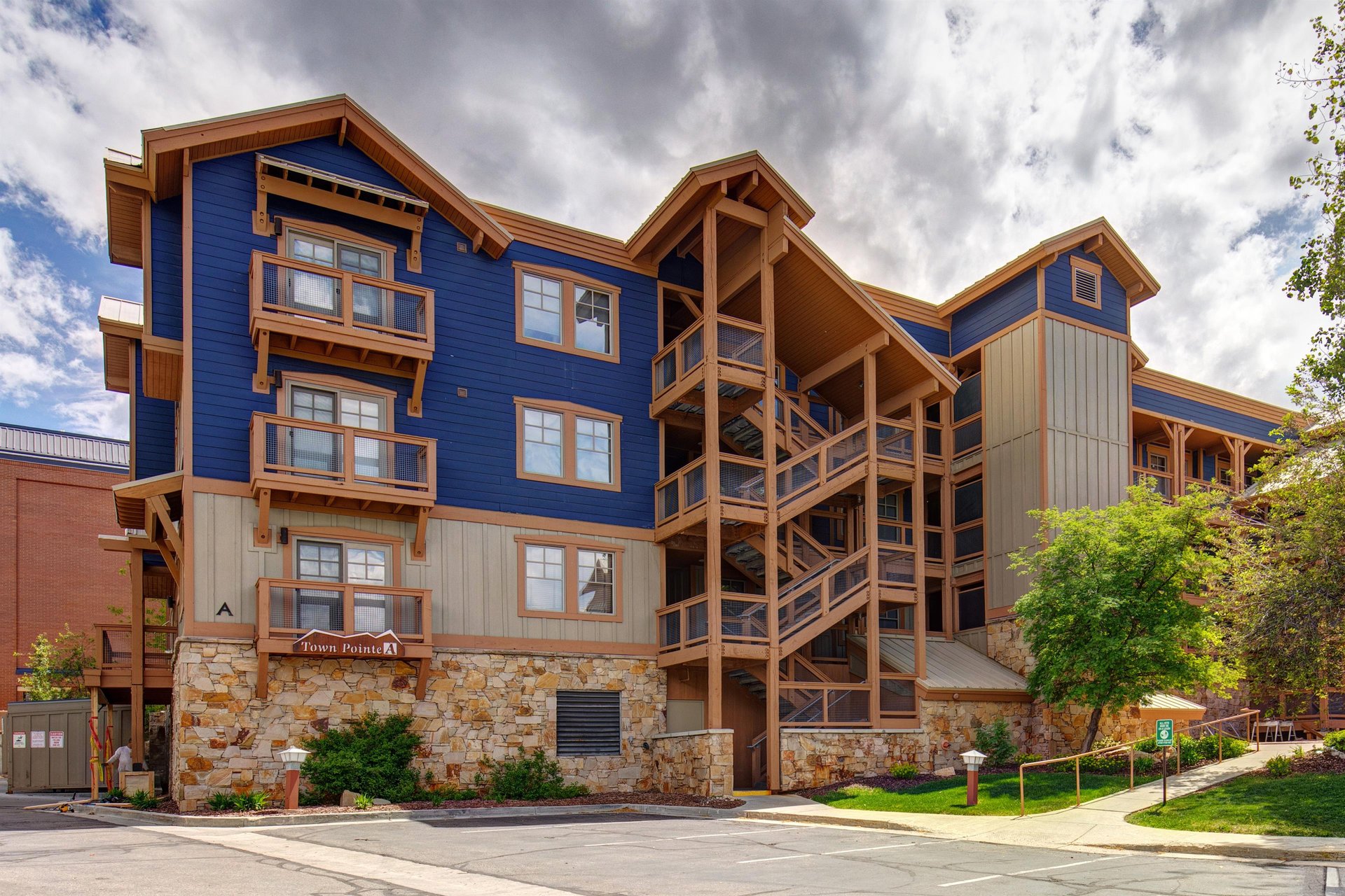 A striking mountainstyle property featuring bold blue siding, natural wood accents, and stone foundation set against dramatic skies—part of the welcoming arrival experience.