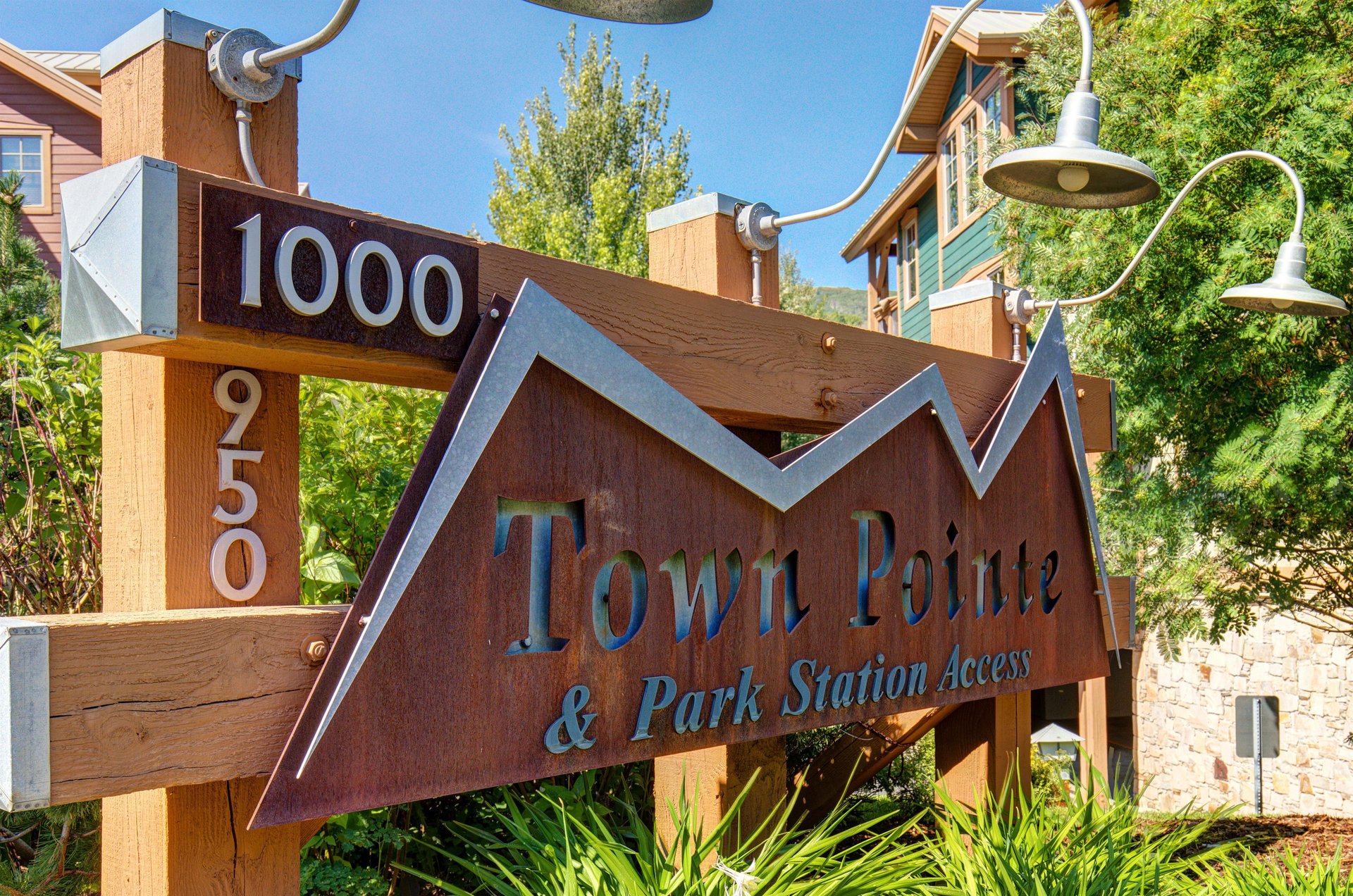 A distinctive wooden sign marks the Town Pointe property entrance at 1000950, featuring decorative lighting and surrounded by lush greenery beneath a clear blue sky.