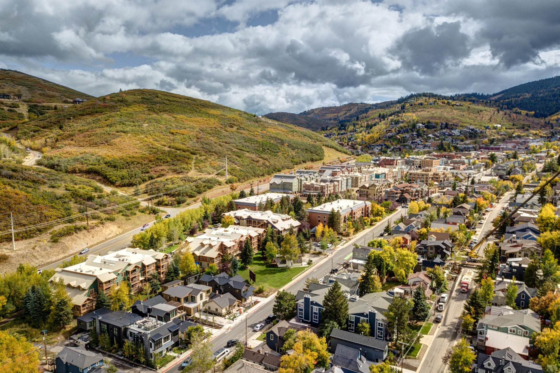 A charming mountain town nestled in a valley, surrounded by rolling hills with autumn foliage and scenic roads winding through the landscape.