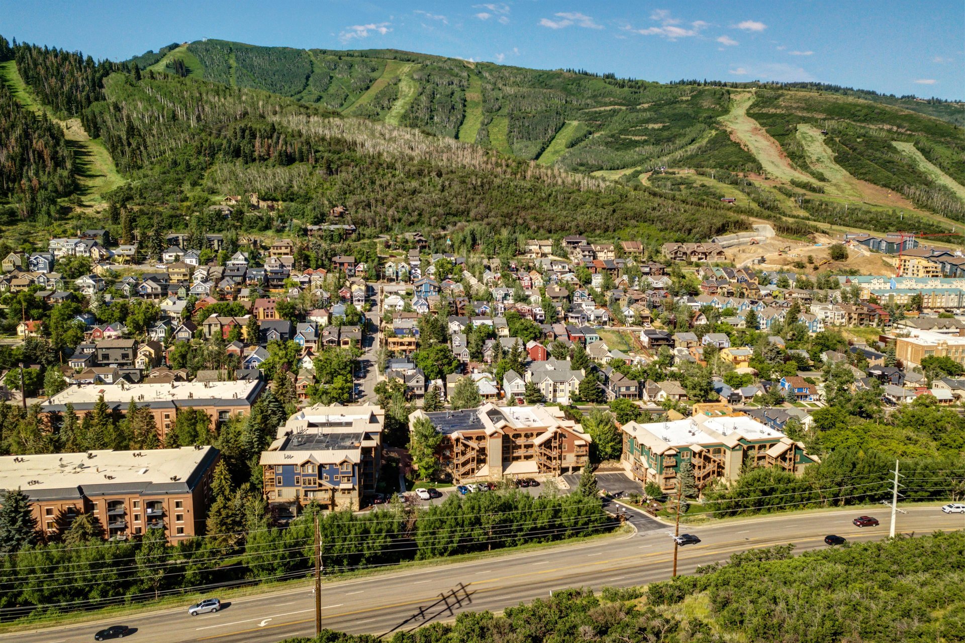 Aerial view of a mountain town nestled at the base of ski slopes, surrounded by forests and open trails winding through the hillside.