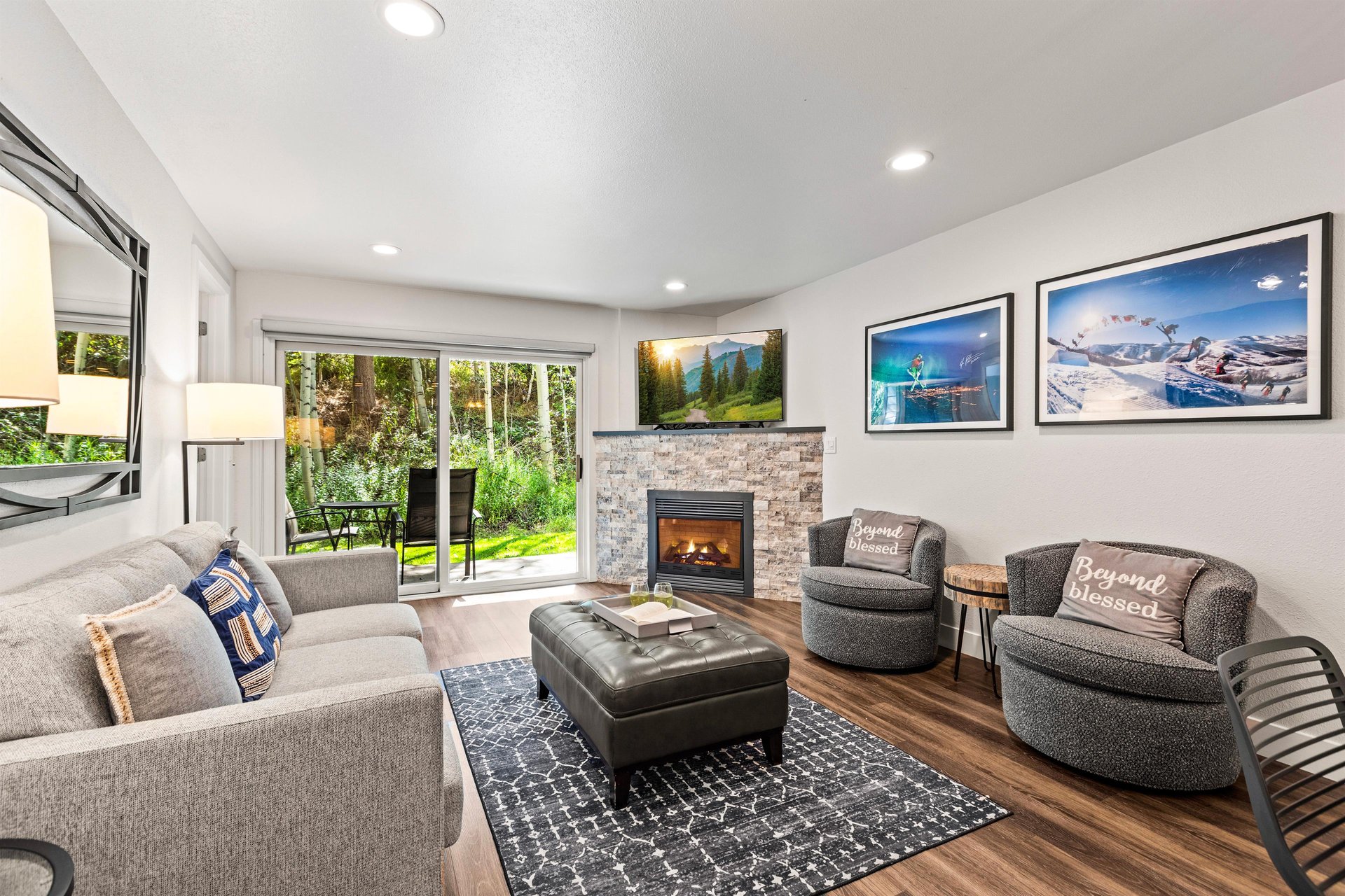 Inviting living room with sofa, swivel chairs, stone fireplace, TV and patio access surrounded by trees