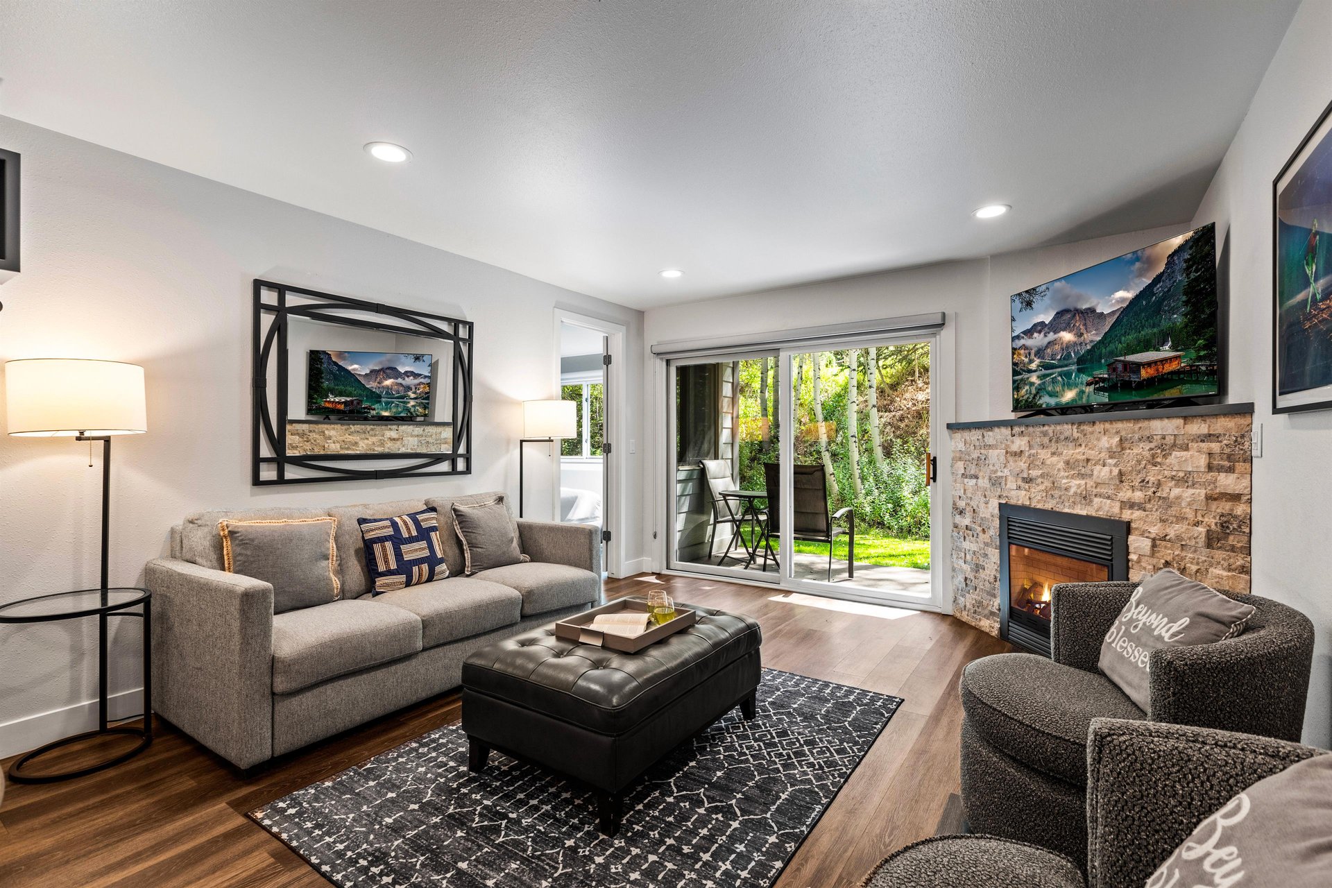 Cozy Park City living room with sofa, stone fireplace, TV and sliding glass doors overlooking aspens