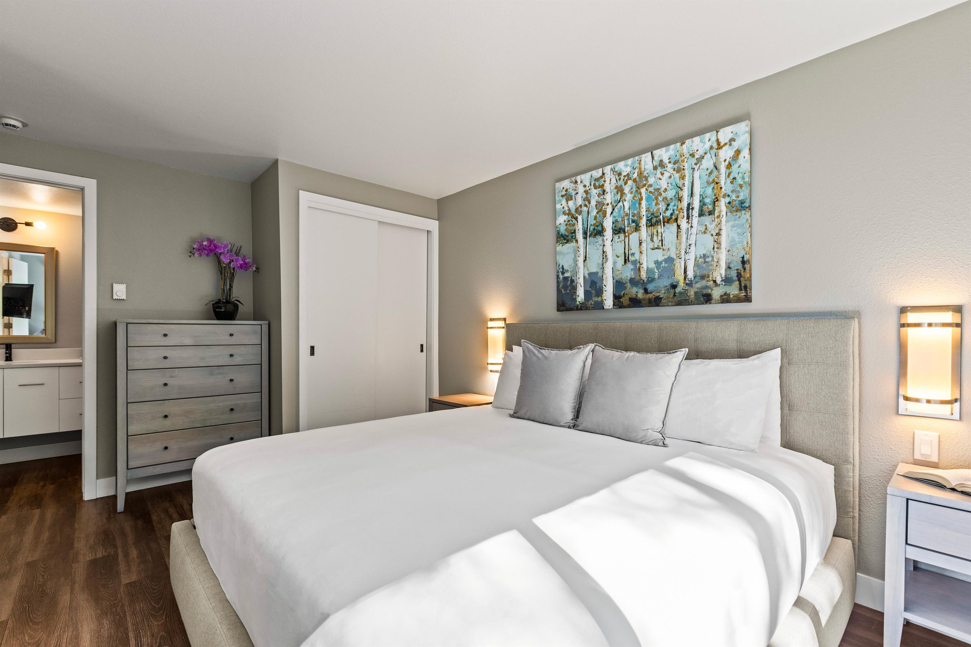 Spacious king bedroom with upholstered bed, dresser, aspen artwork and ensuite bathroom