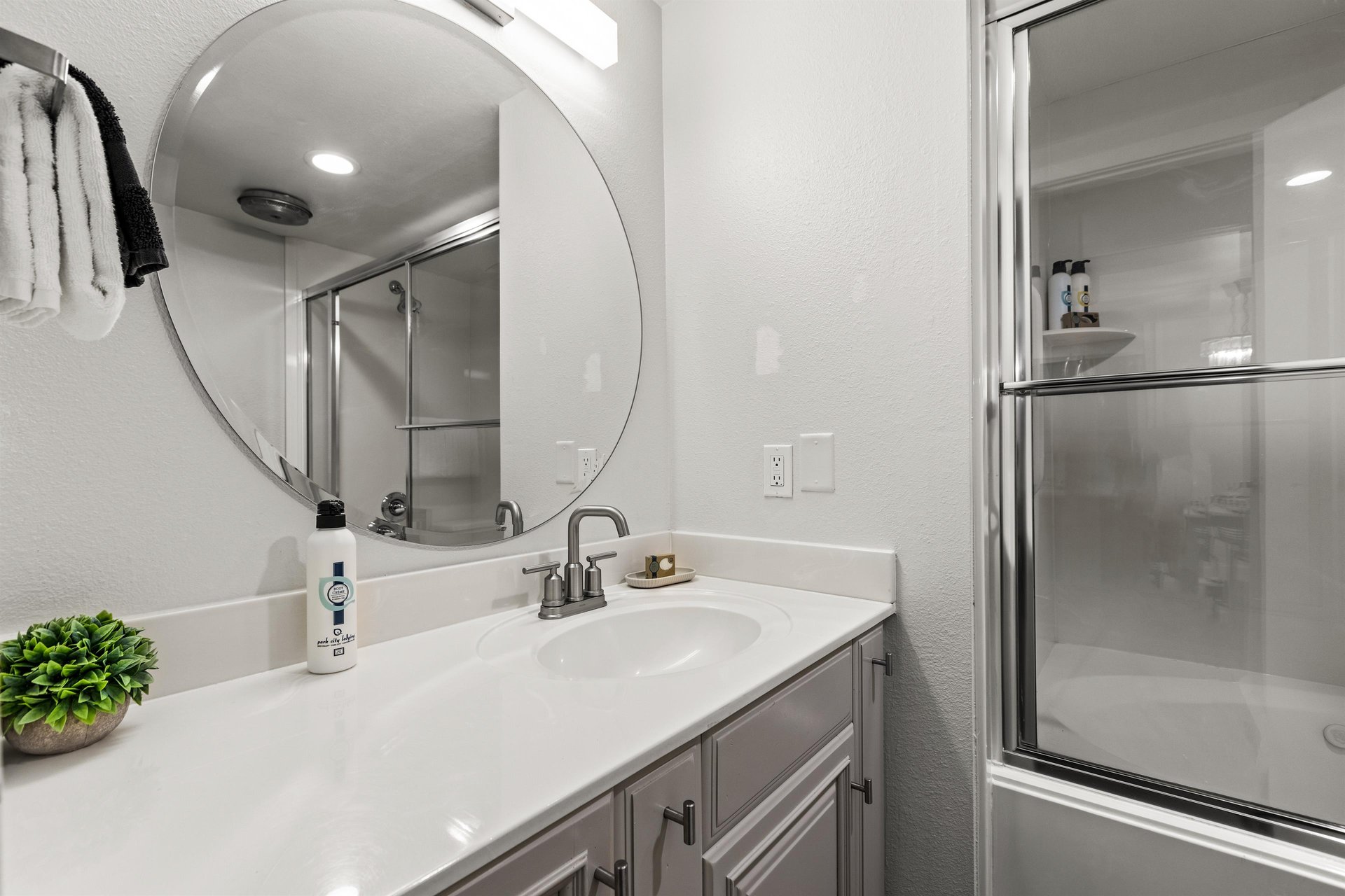 Secondary bathroom with spacious vanity, round mirror and tubshower combination with glass doors