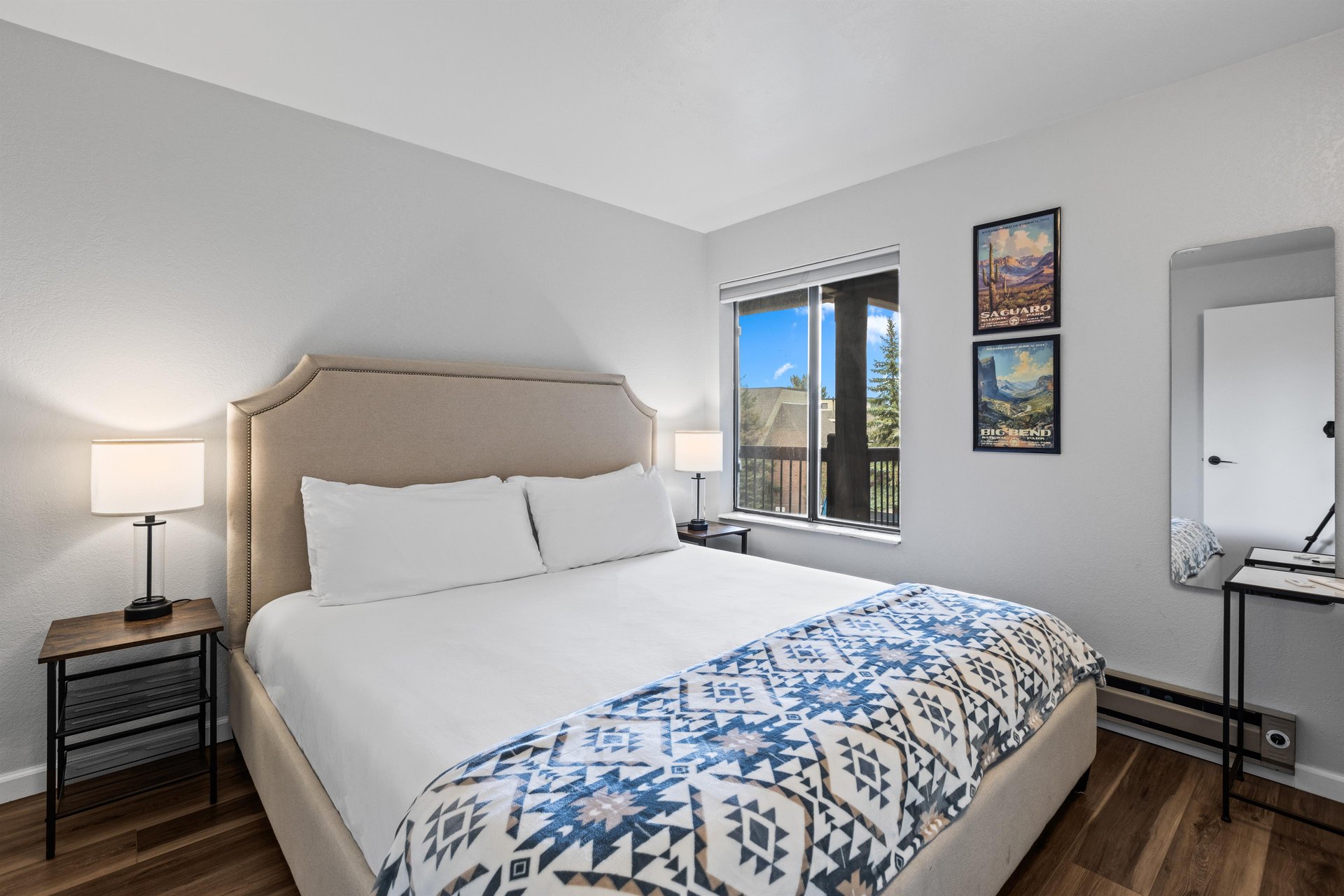 The bedroom offers a king size bed with an upholstered headboard and two end tables with lamps.