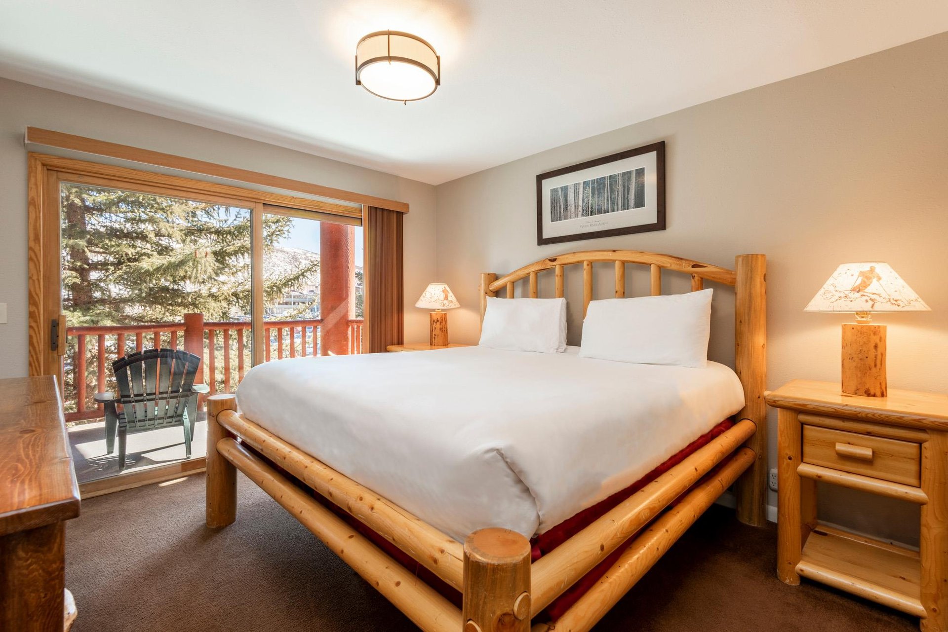 Cozy main bedroom with logframe bed, white bedding and large windows overlooking the trees