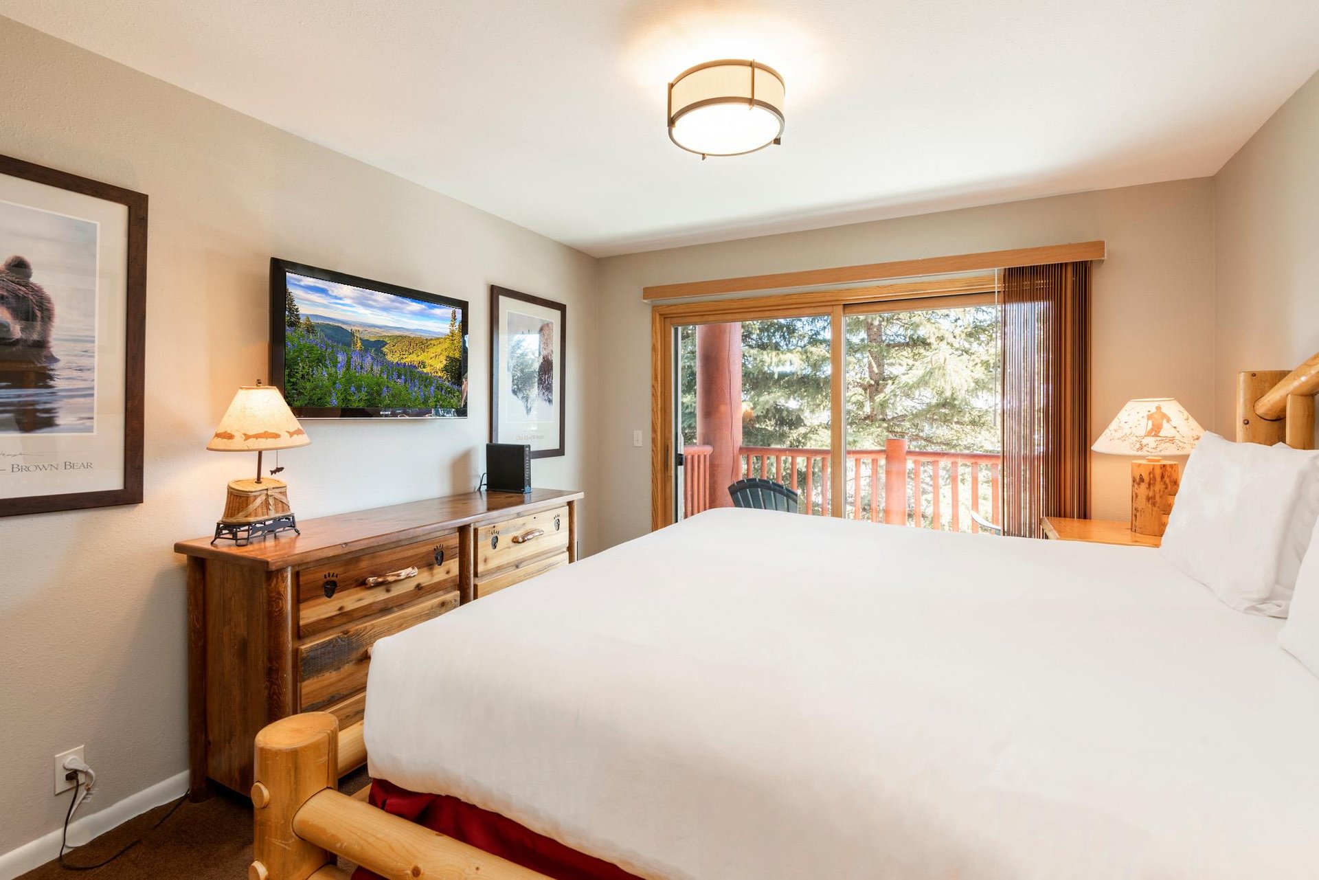 Main bedroom with logframe bed, flatscreen TV and large windows opening to a private treelined balcony