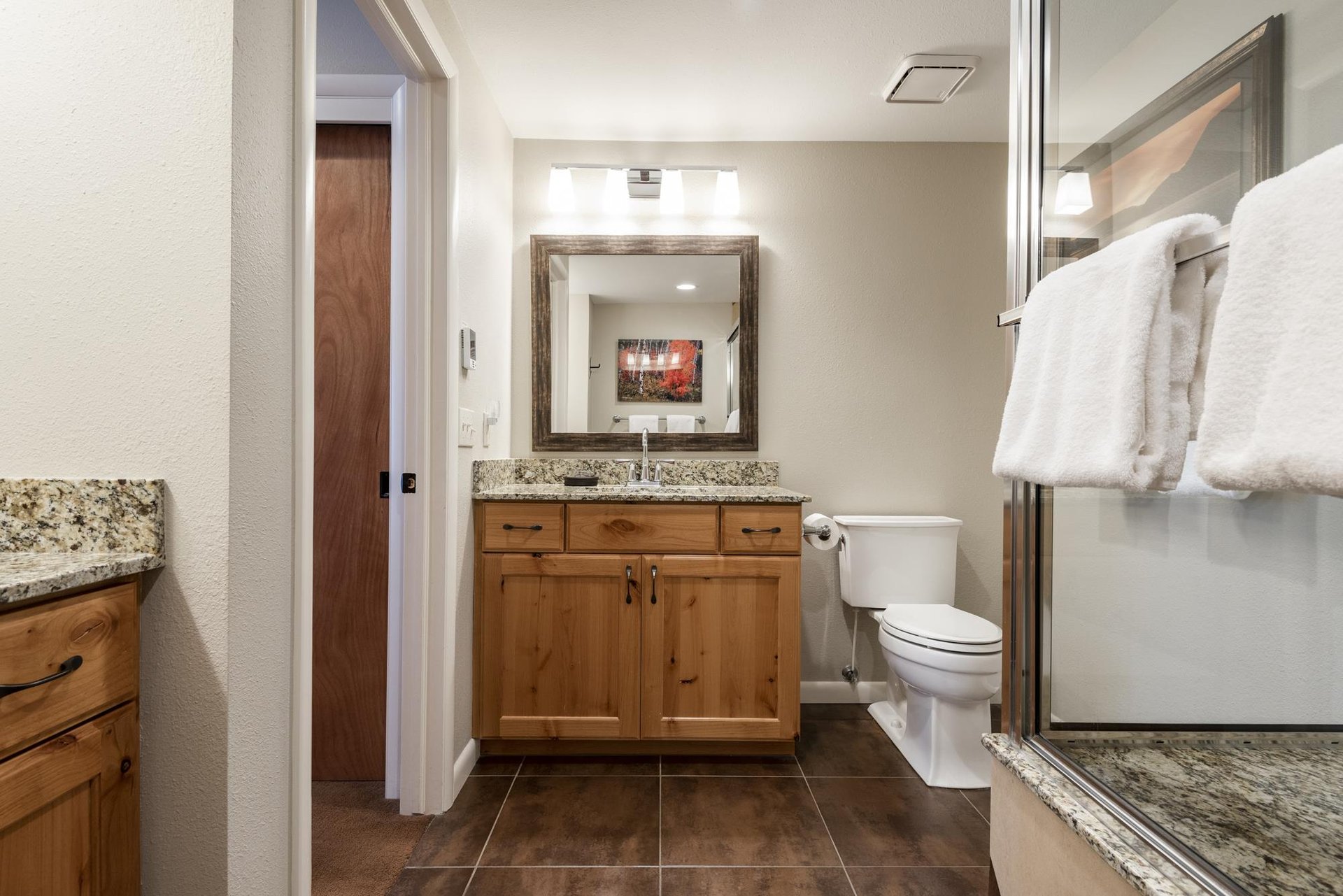 Ensuite main bathroom with wood vanity, tiled floors, toilet and glassenclosed shower