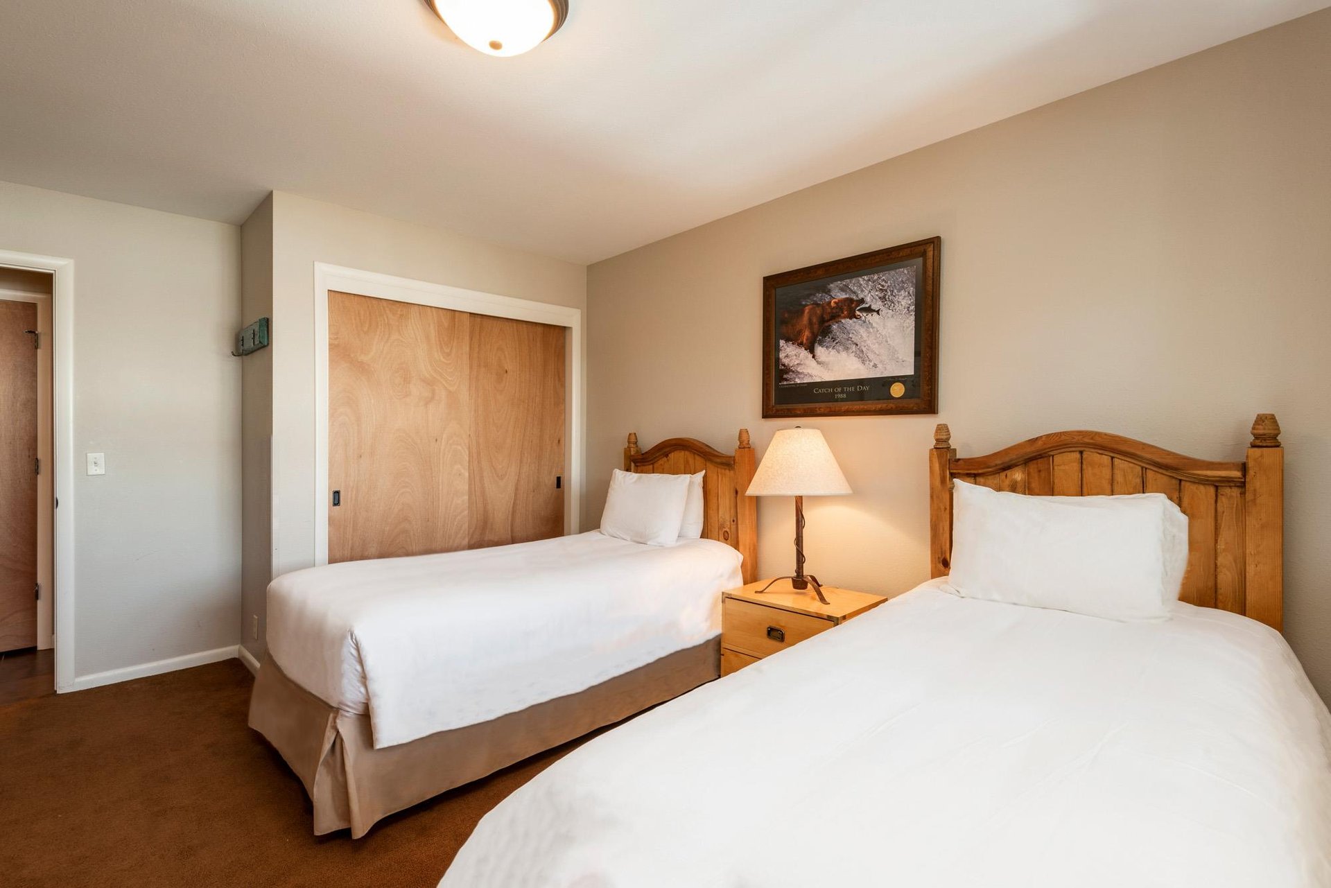 Comfortable guest bedroom with two beds, wood headboards, bedside table and warm mountainstyle décor