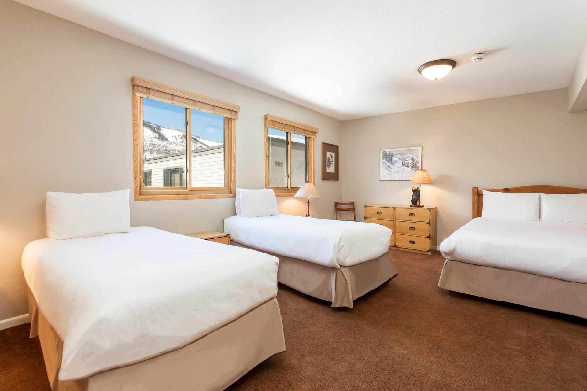 Spacious open loft sleeping area with three beds, wood furnishings and large windows with natural light
