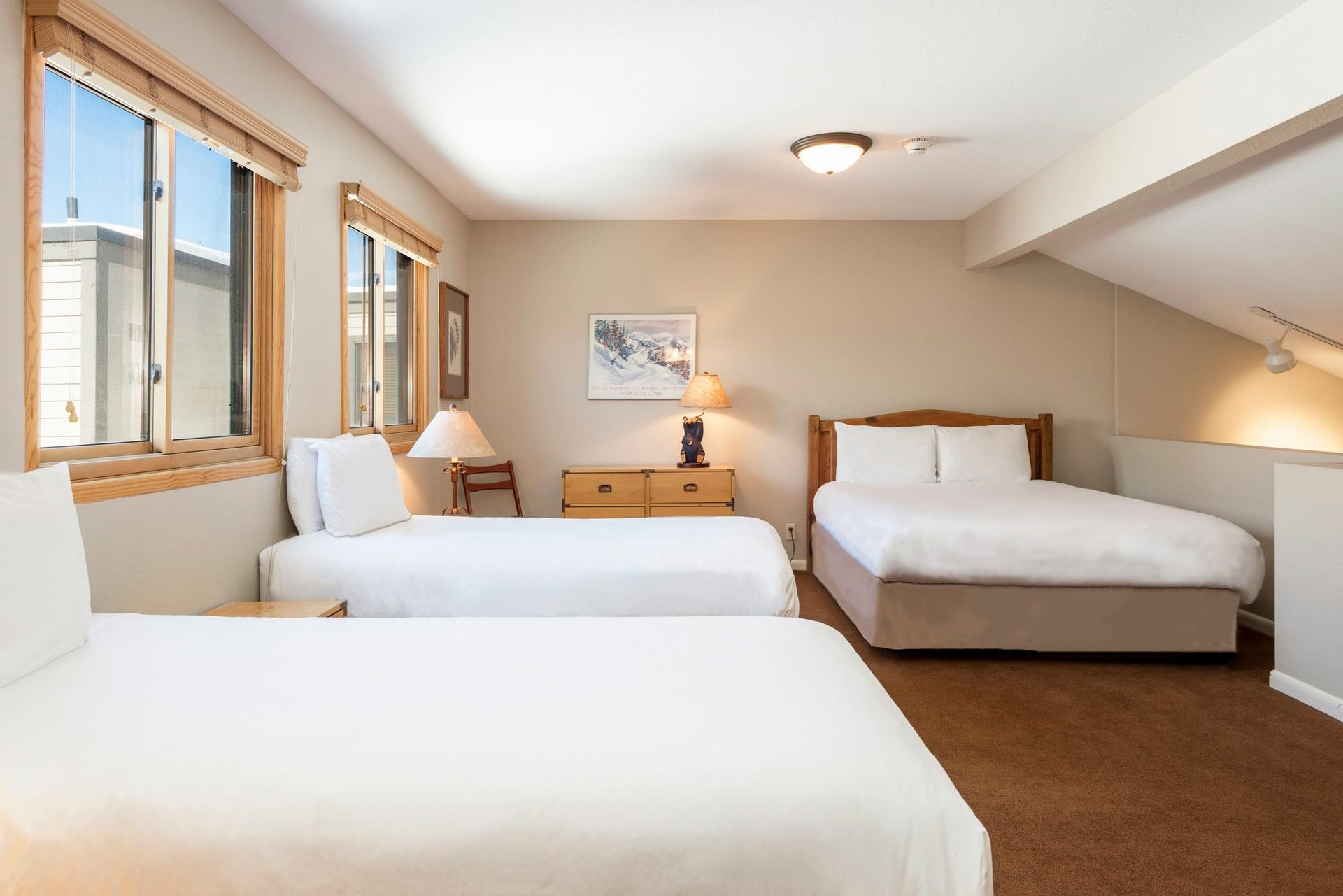 Open loft sleeping area with two twin beds, one queen bed, wood furnishings and large windows with natural light