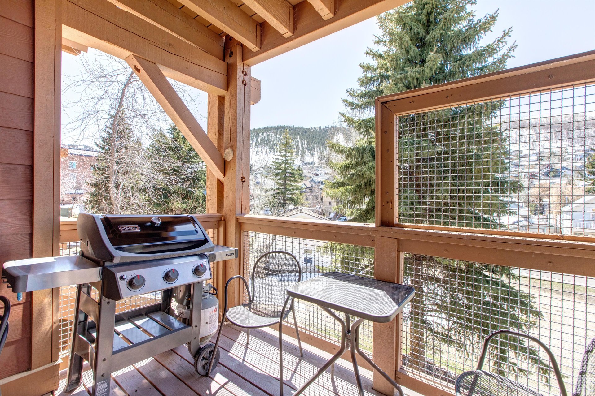Covered private patio with gas BBQ grill, outdoor table, seating and mountain views.