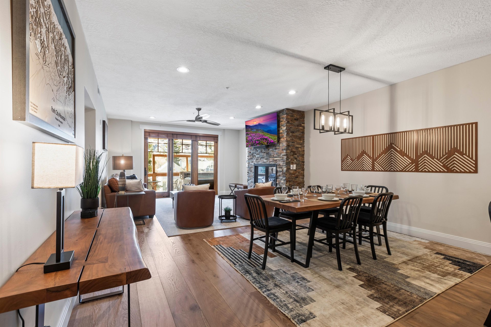 Open dining area with wood table for six, modern chandelier, wood floors and views of the stone fireplace and patio.