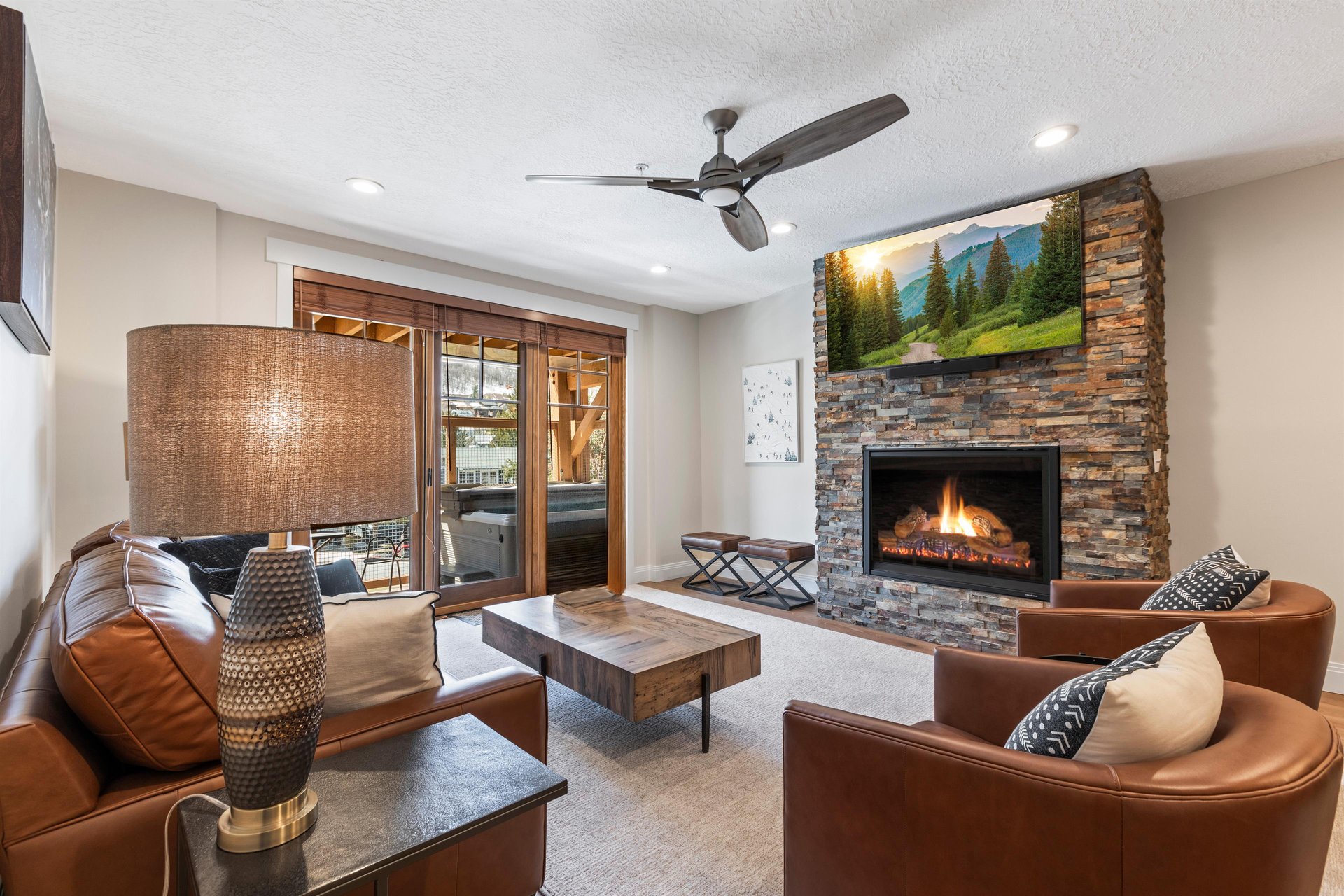 Beautifully designed living room with leather seating, stone fireplace, TV and doors opening to the outdoor patio.