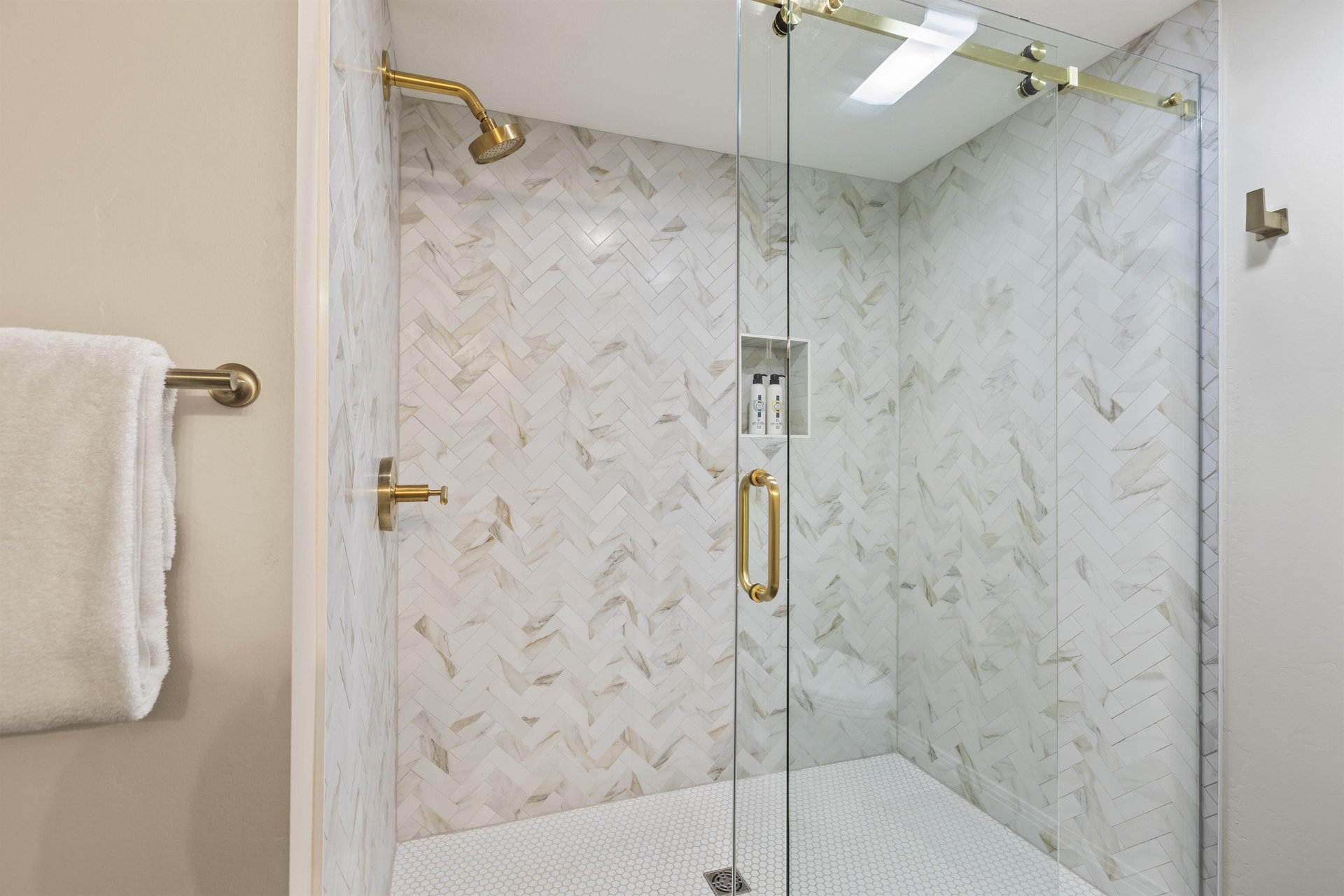 Ensuite bathroom with glassenclosed walkin shower, marblepatterned tile, builtin bench and gold fixtures.