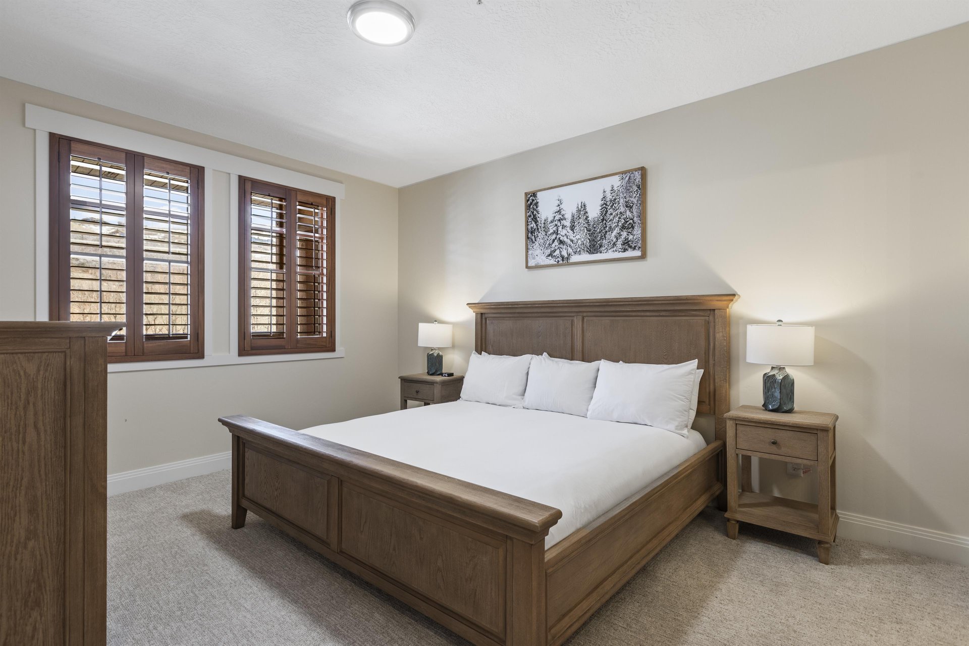 Spacious second main bedroom with wood king bed, matching nightstands, bedside lamps and windows with wood shutters.