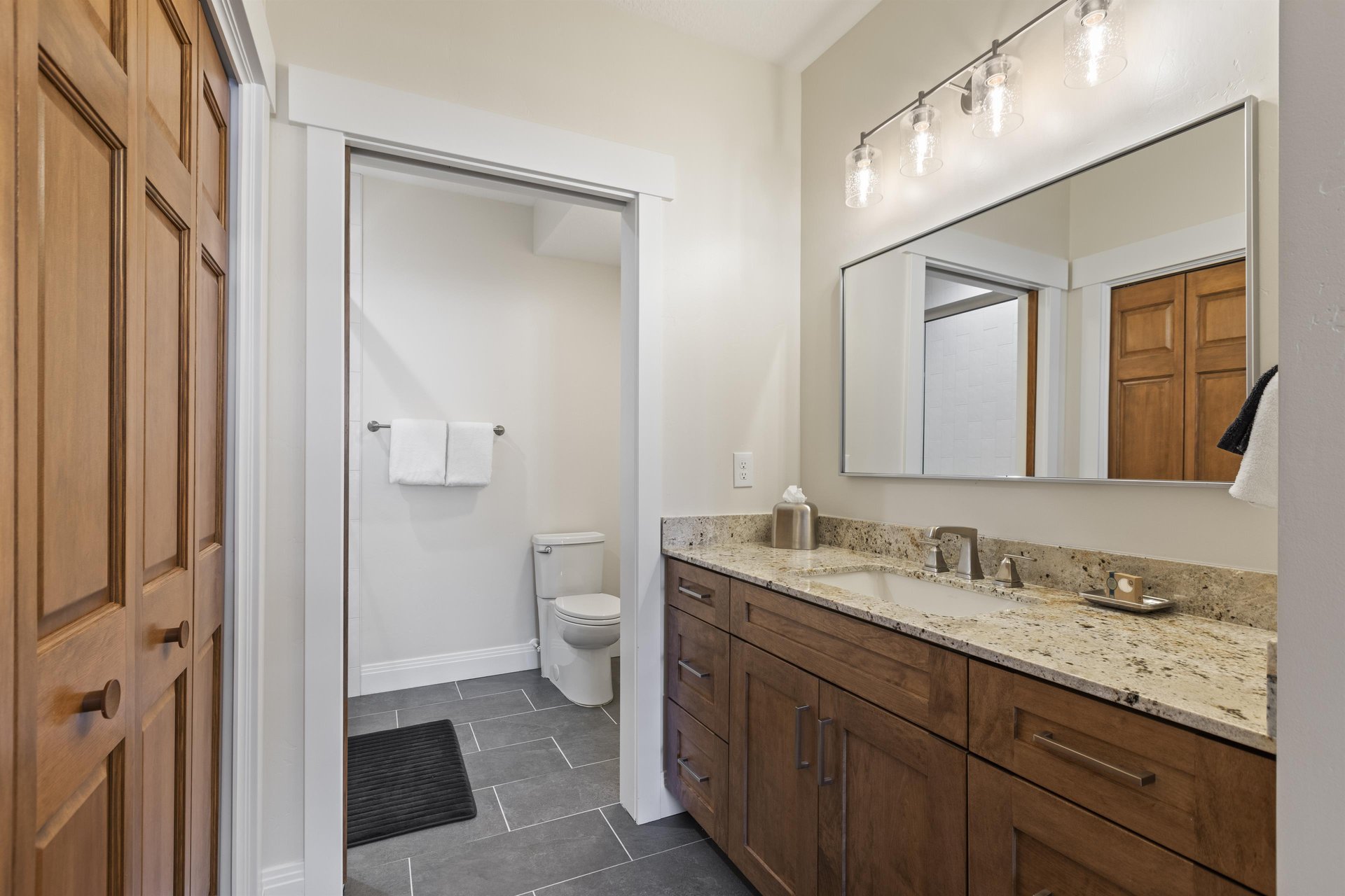 Ensuite bathroom with granite double vanity, wood cabinetry, large mirror, tile flooring and separate toilet area.