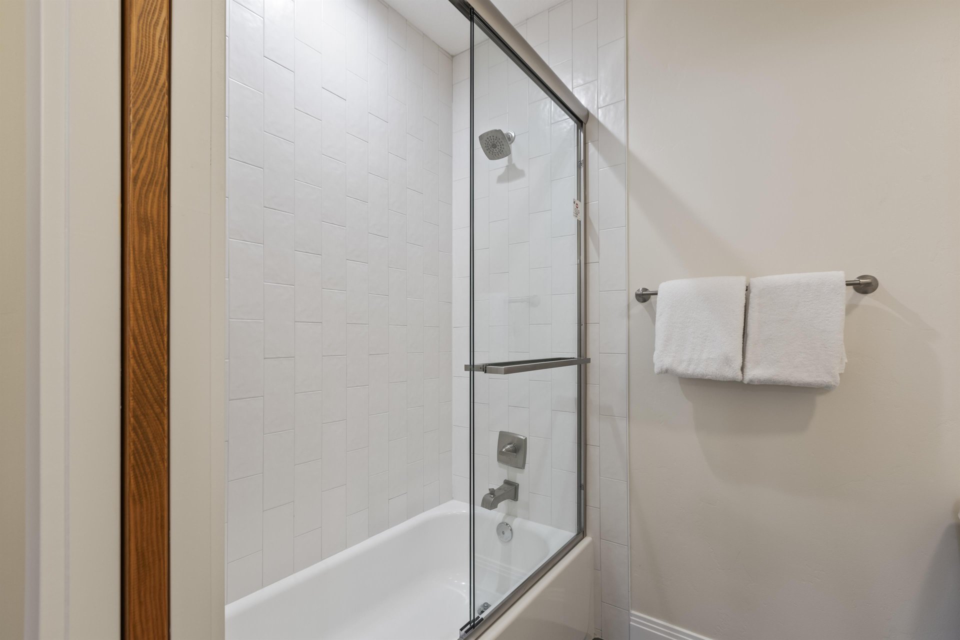 Ensuite bathroom with a shower and tub combination, white tile surround, glass shower door and builtin shelving.