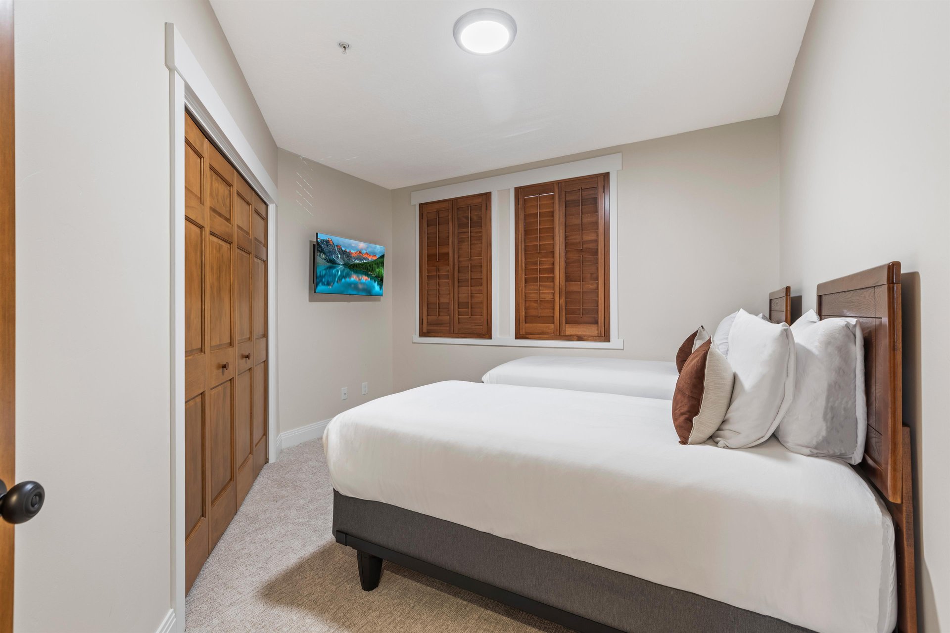 Third bedroom with two twin beds convertible to a king, wood closet doors, wallmounted TV and shuttered windows.