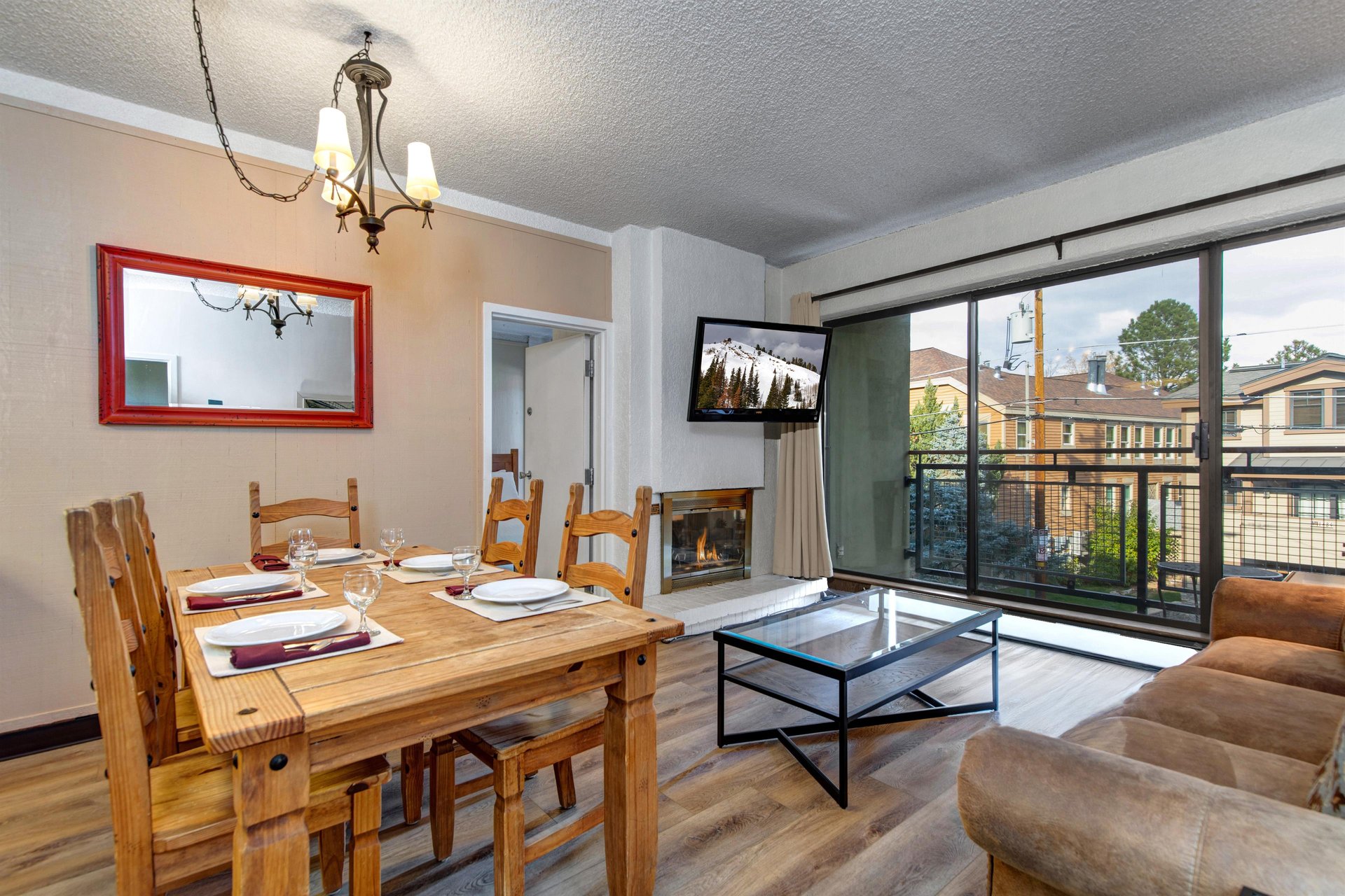 Open living and dining area with wood table, gas fireplace, wallmounted TV and large windows with mountain views.