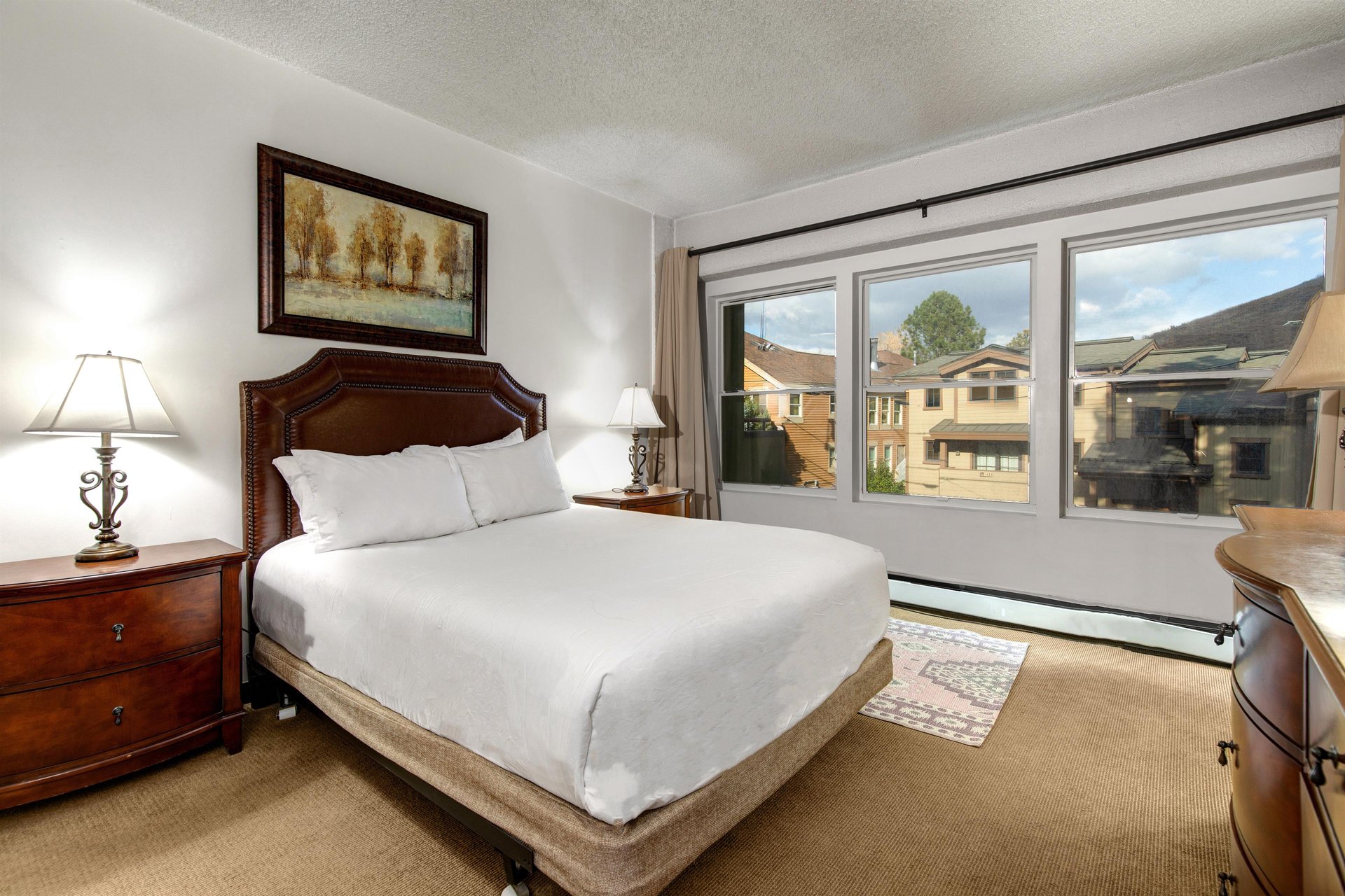 Bright bedroom with queen bed, wood headboard, bedside tables and large window with mountain views.