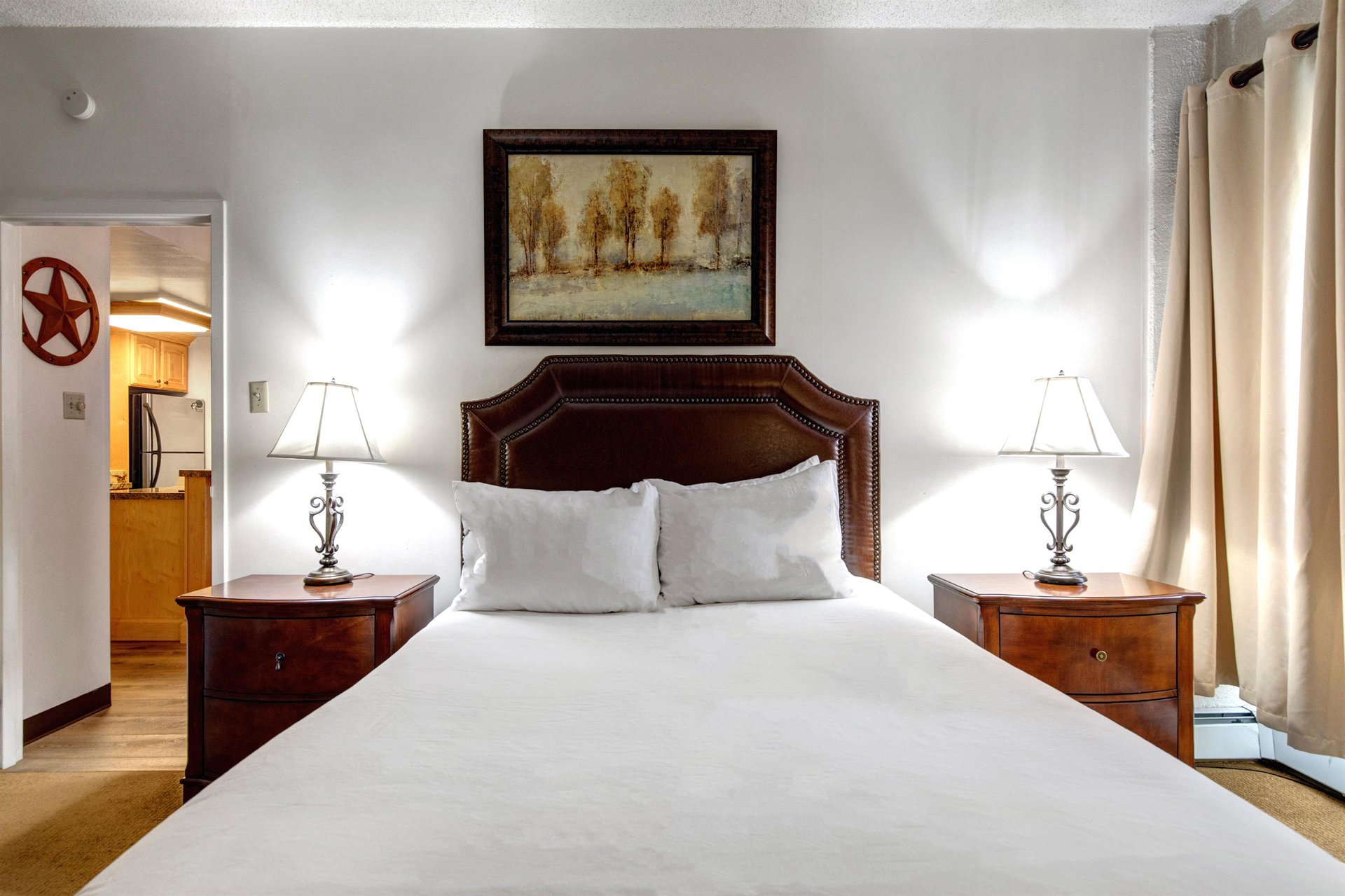 Comfortable bedroom with queen bed, wood headboard, matching nightstands, bedside lamps and mountaininspired artwork.