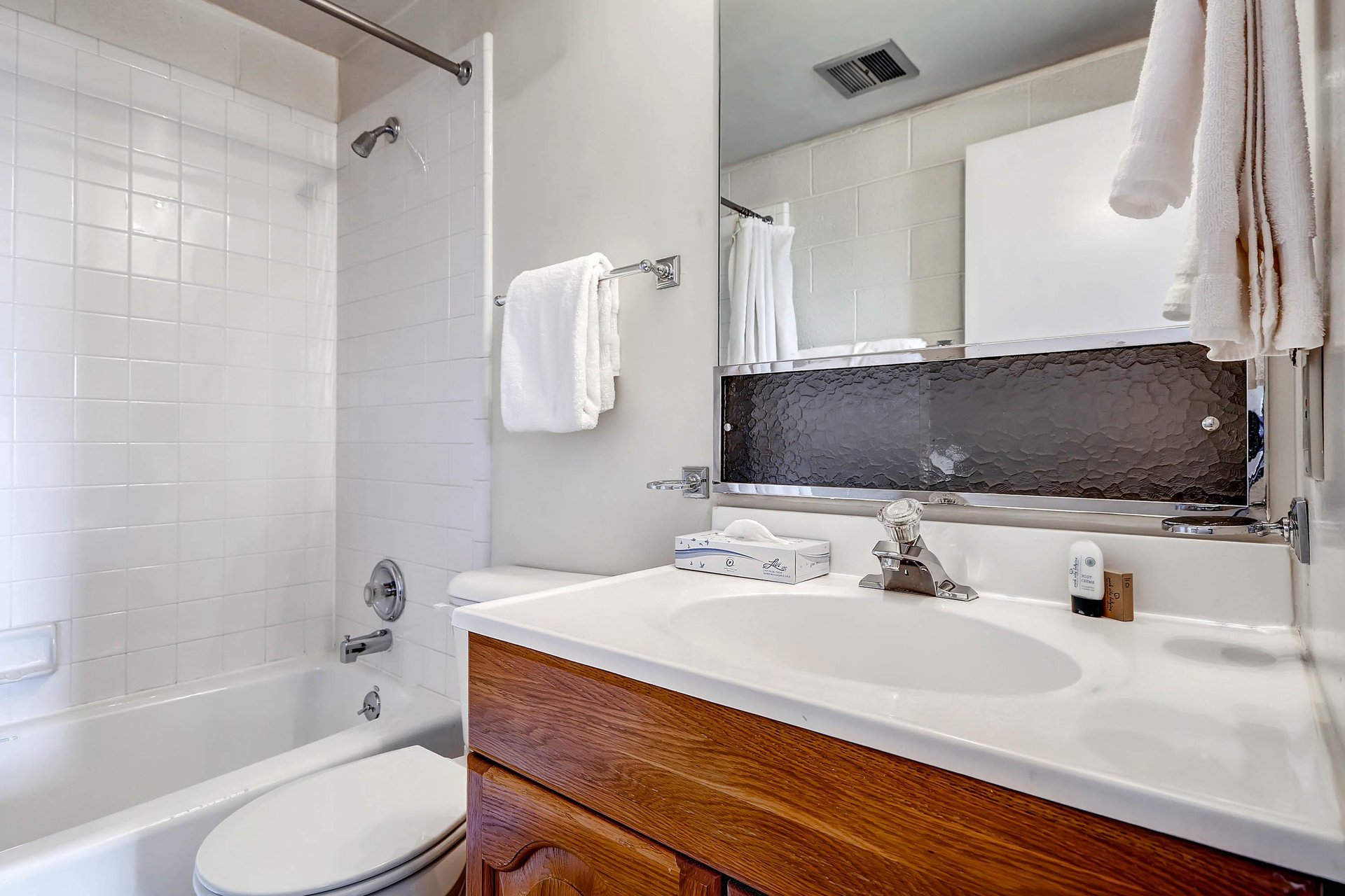 Full bathroom with wood vanity, large mirror and showertub combination with white tile surround.