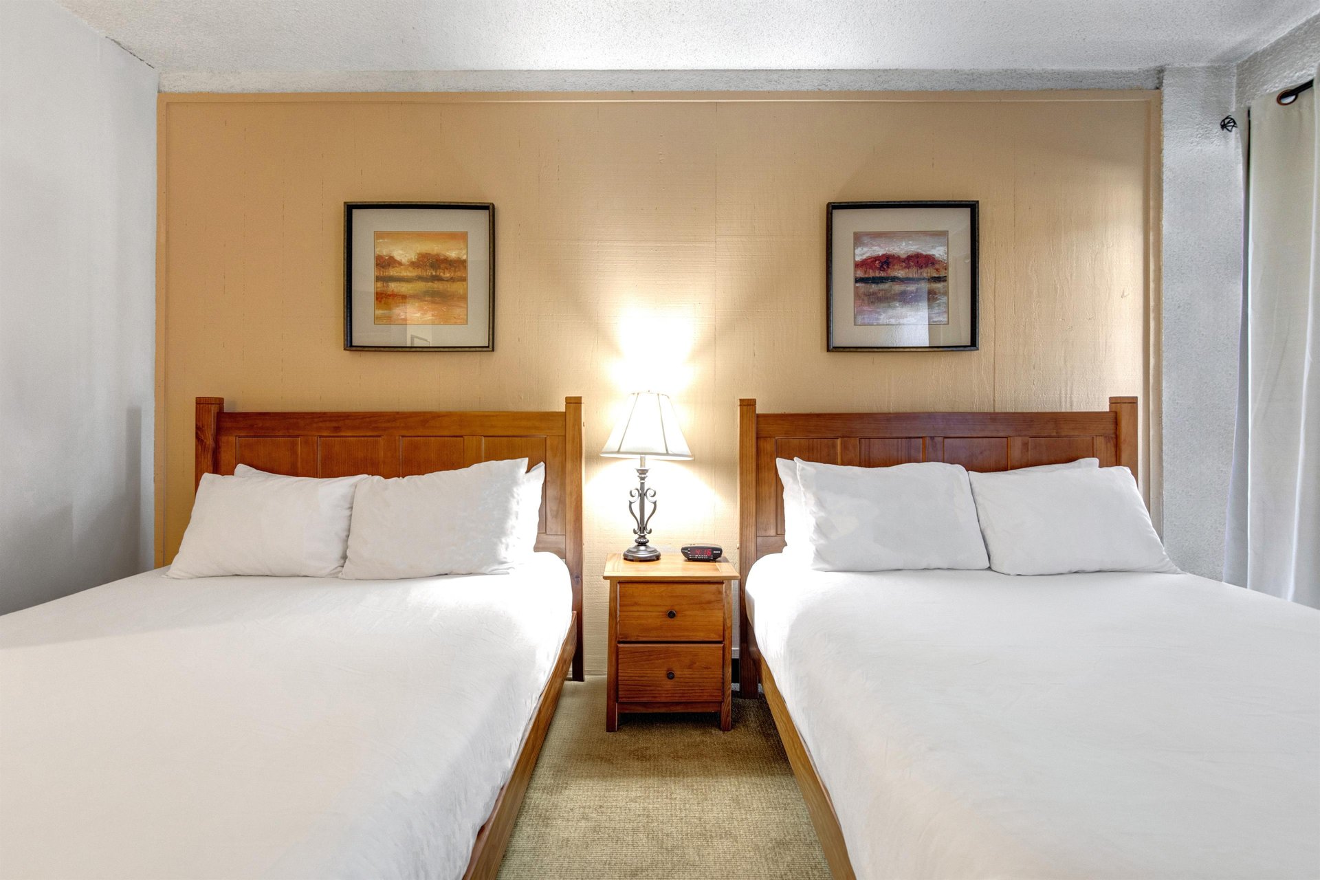 Second bedroom with two queen beds, wood headboards, shared nightstand and individual bedside lighting.