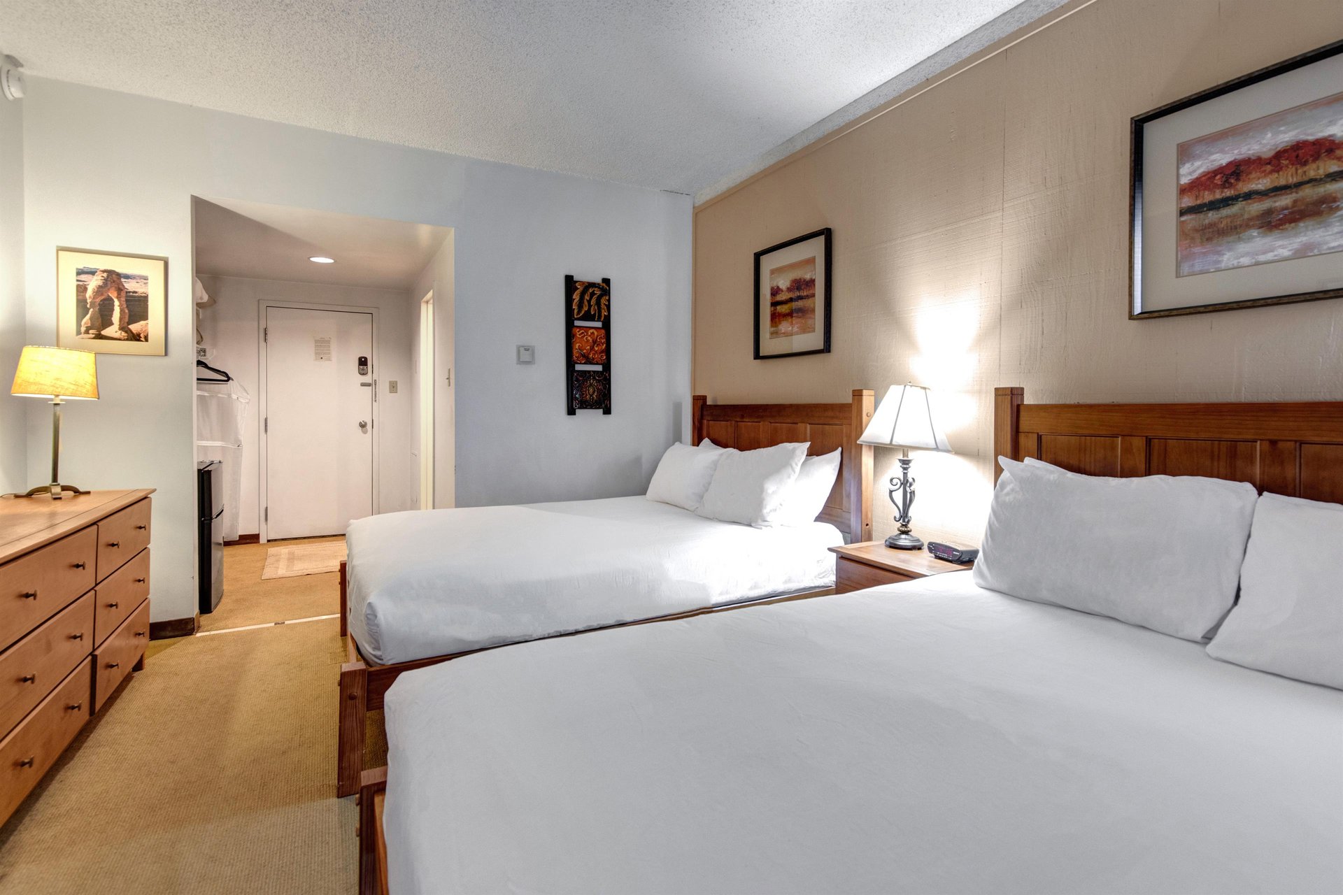 Spacious bedroom with two queen beds, matching wood headboards, bedside lighting and open entry area.
