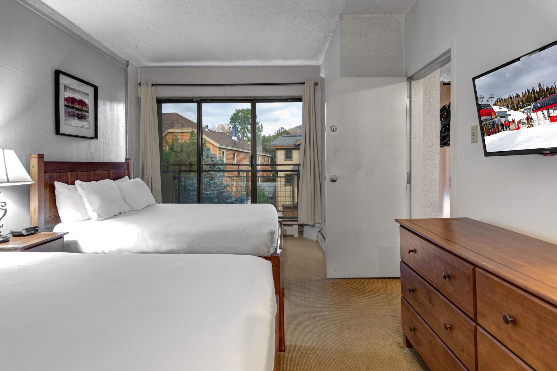 Bedroom with two queen beds, wood dresser and sliding glass door providing natural light and outdoor access.