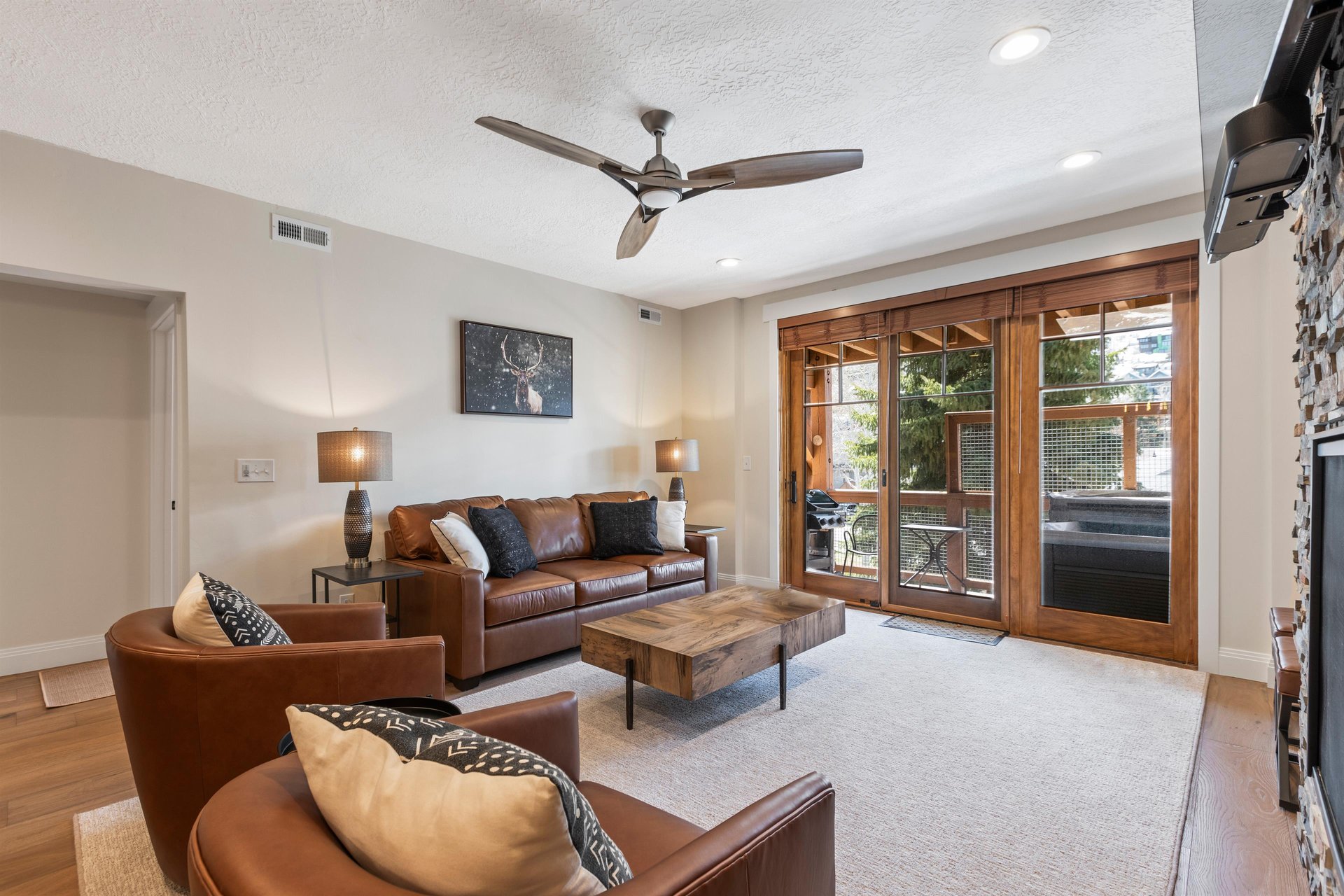 Cozy living room with leather seating, rustic wood coffee table, ceiling fan and glass doors leading to the private patio.