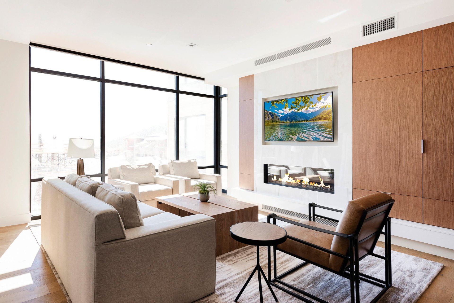 Bright living room with floortoceiling windows, modern fireplace, wallmounted TV and comfortable seating.