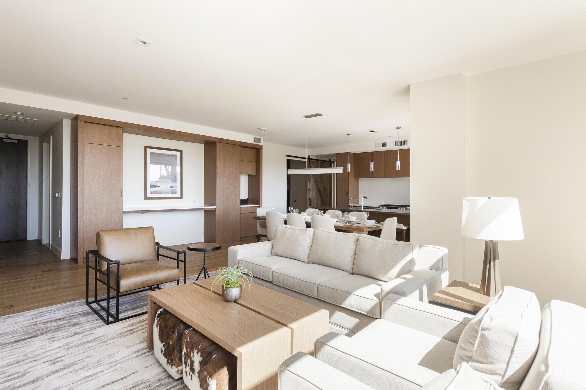 Bright living room with solid wood coffee table, white couch and leather accent chair, with dining and kitchen in the background.