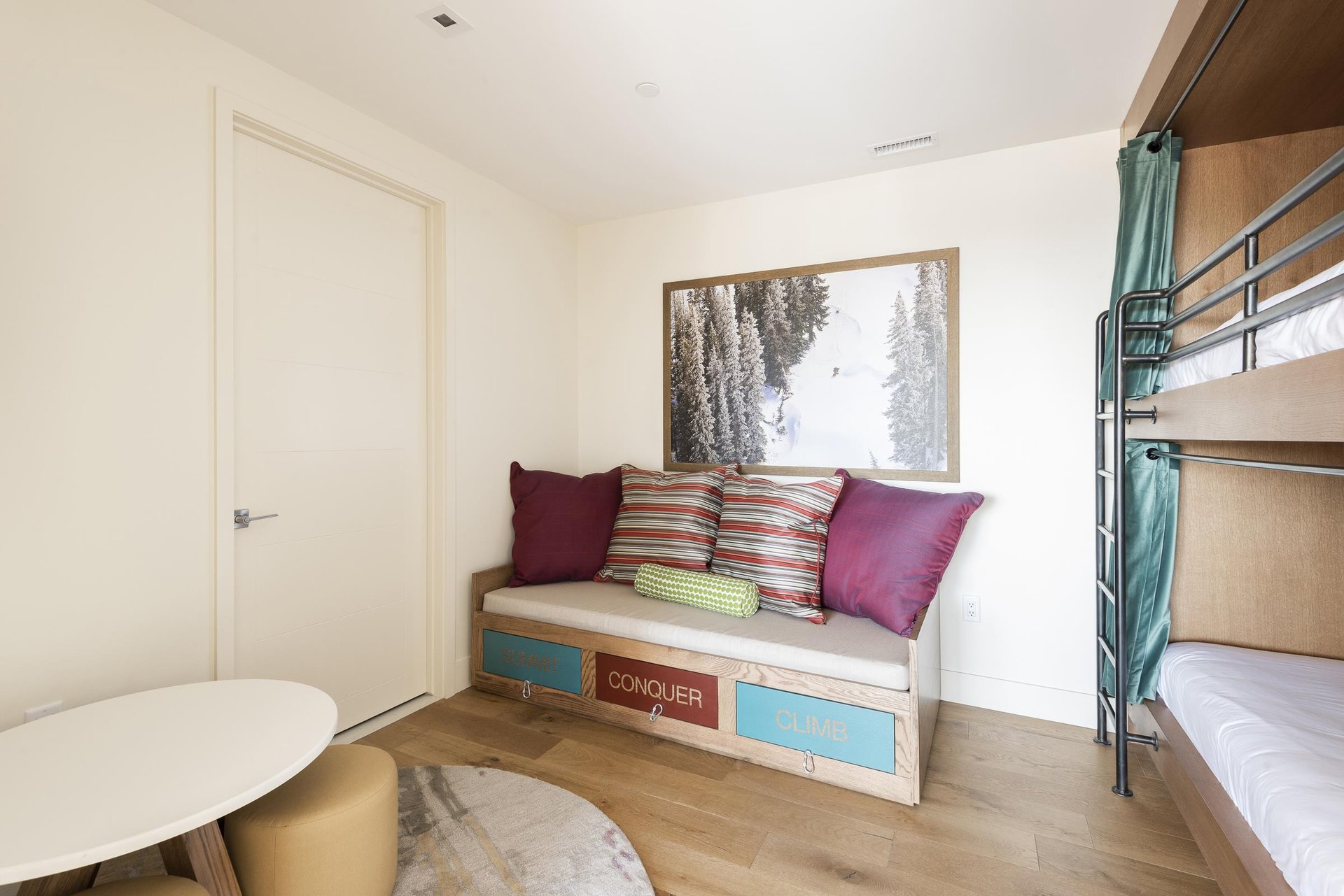 Fun lounge sofa in the bunk bedroom with colorful throw pillows, mountain inspired wall art, and round play table.