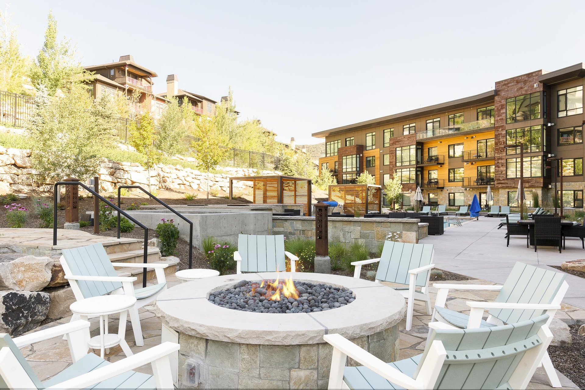 The Lift Condominiums outdoor circular firepit with white wooden Adirondack chairs, perfect for apres ski relaxation.