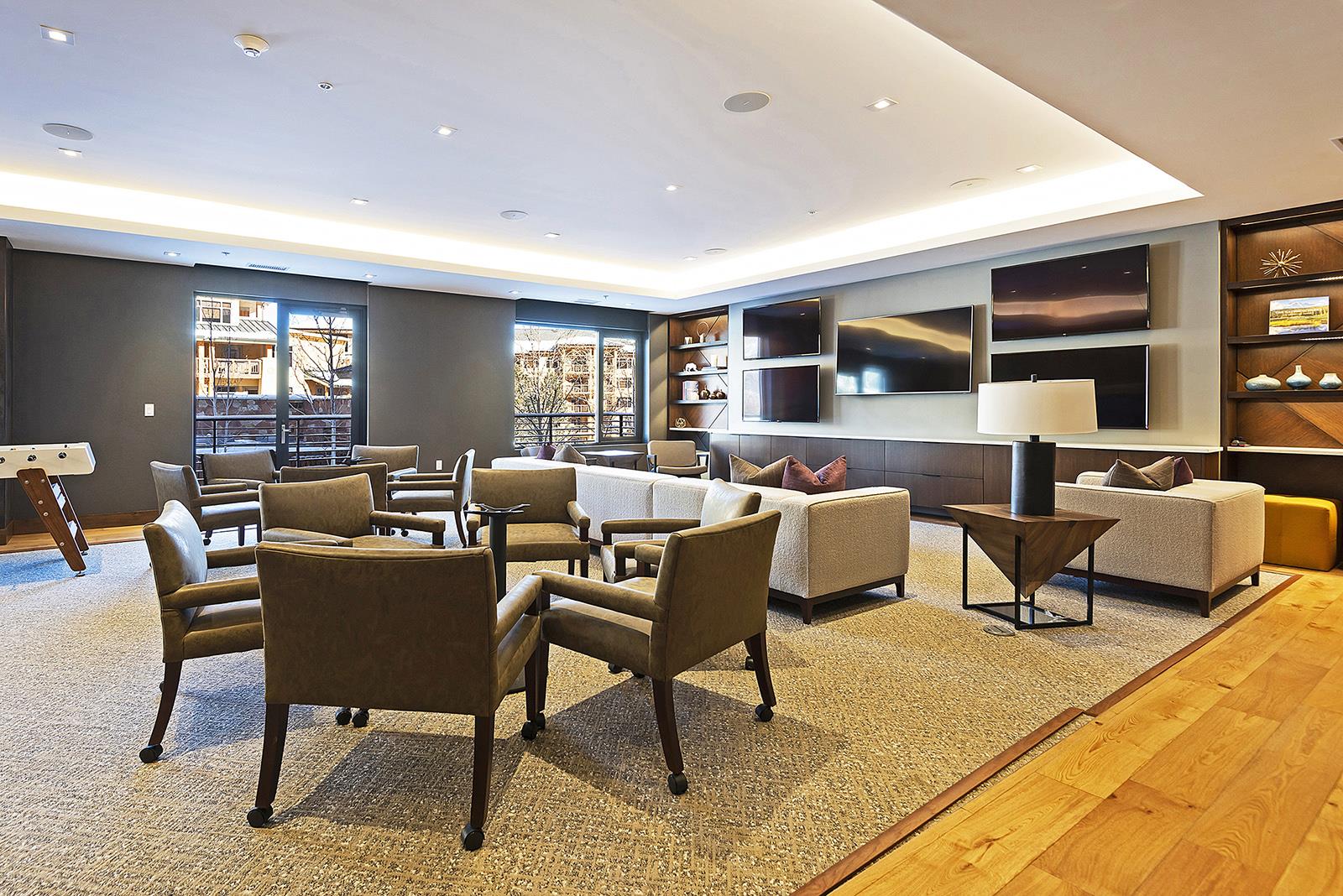 Hardwood and carpeted floor in the club room with various leather armchairs for seating and TVs and large sofa in the background