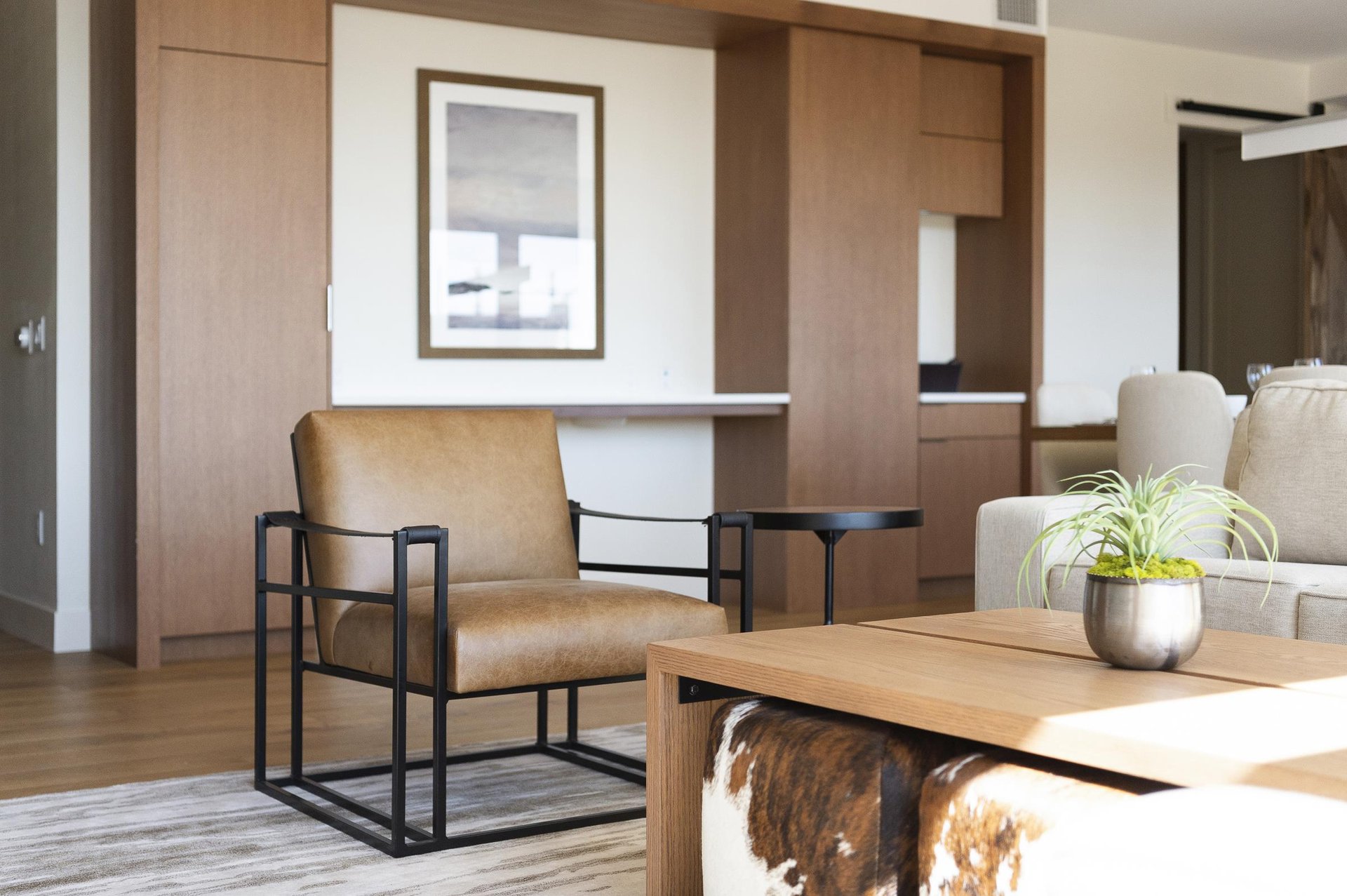 Unique modern mountain design, leather and iron accent chair in the living room, wooden coffee table, and cowhide cube poufs.