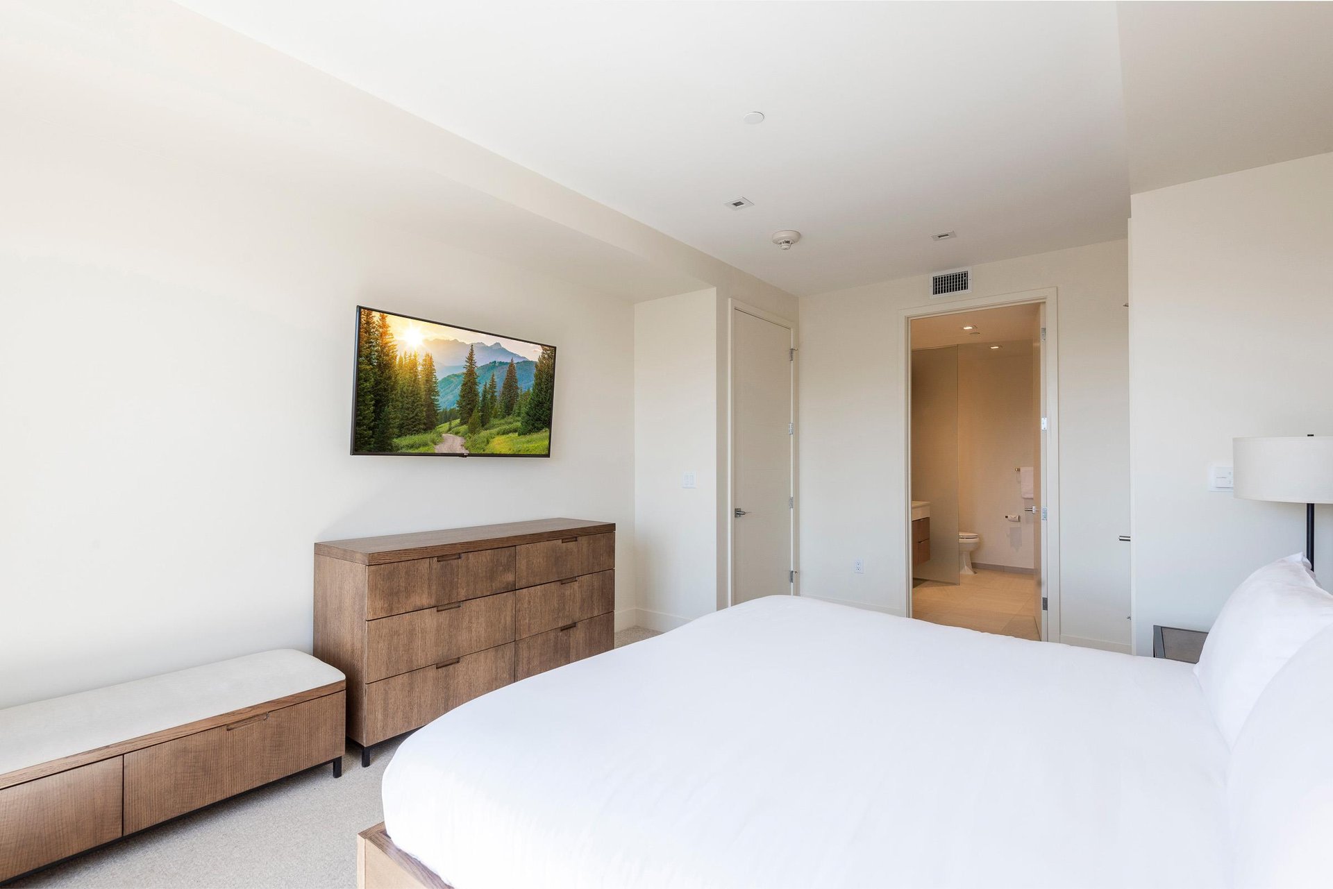Spacious main bedroom suite with king bed, wooden dressers and woodsuede bench with wall mounted flat screen TV.