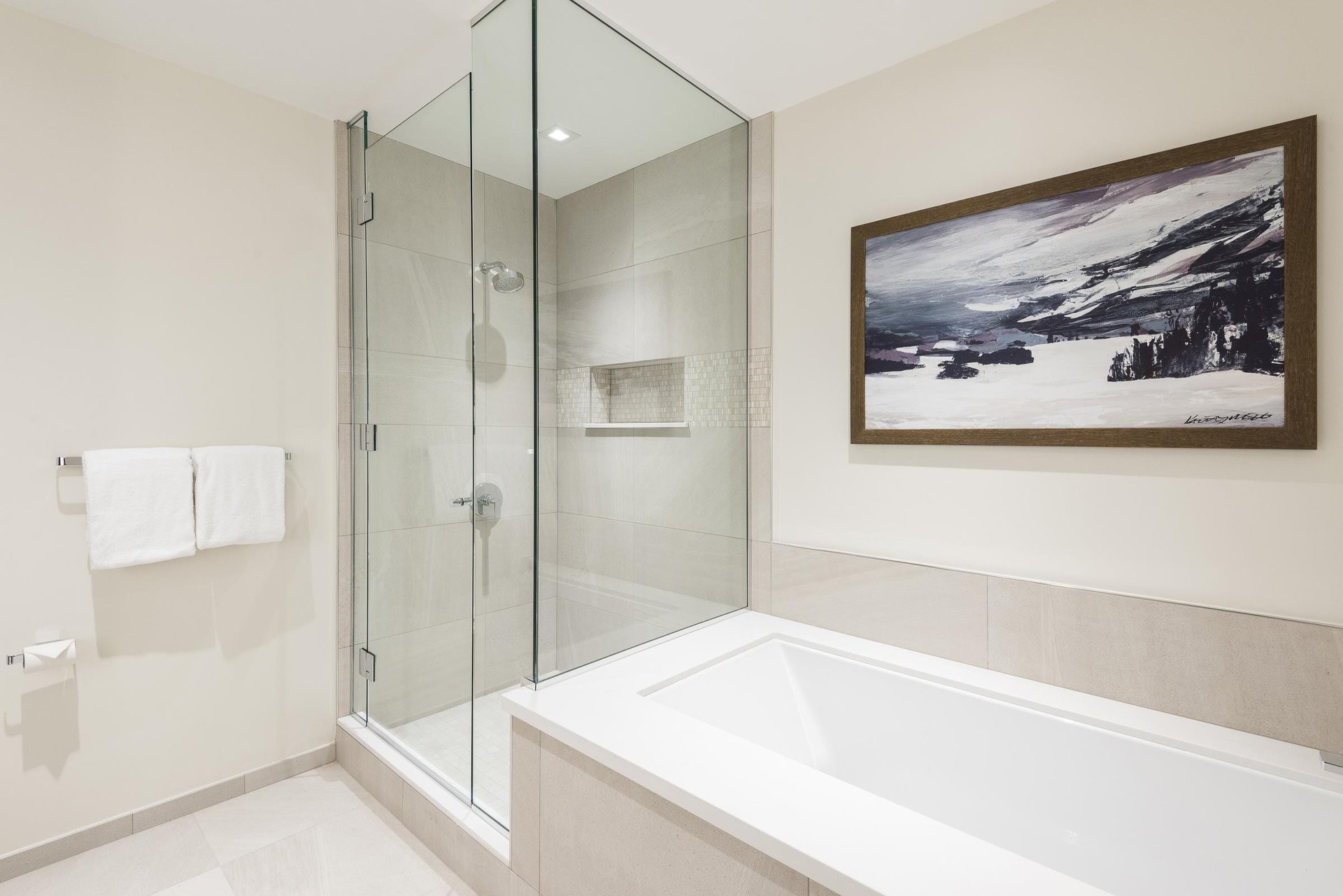Main bathroom with deep soaking tub, mountain art, and glass paneled shower.