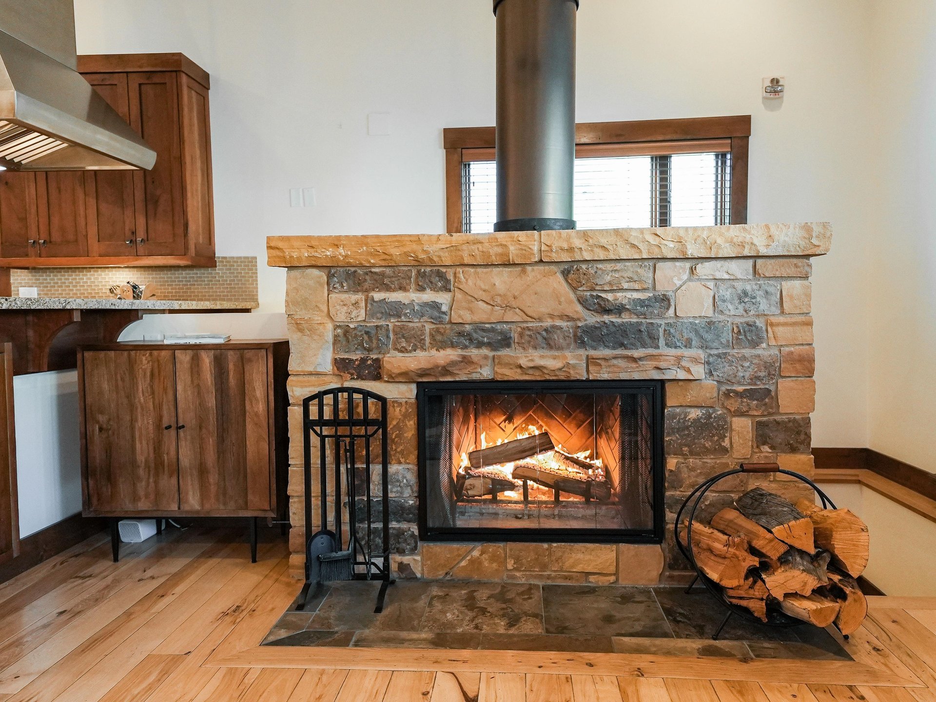 The wood burning fireplace with stone surround, firewood bundled in metal holder, and fire tools.