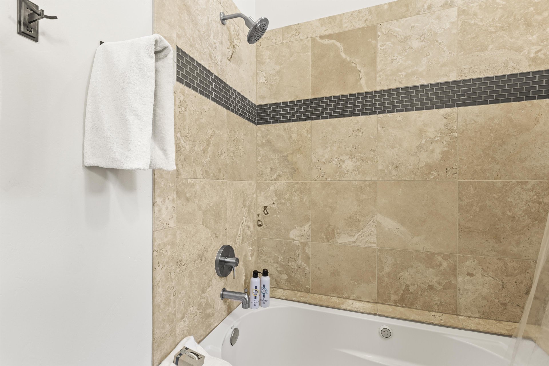 The shared bathroom has a white bathtub and cream tile surround with grey inlayed tile.