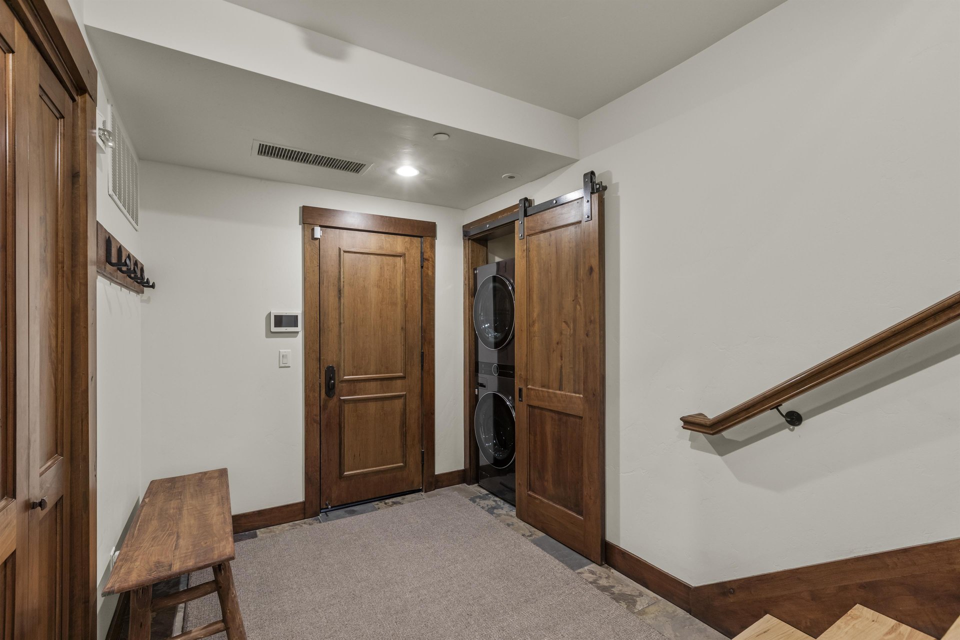 The spacious entry way has a bench to remove shoes and a stacked washer and dryer behind a barn door.