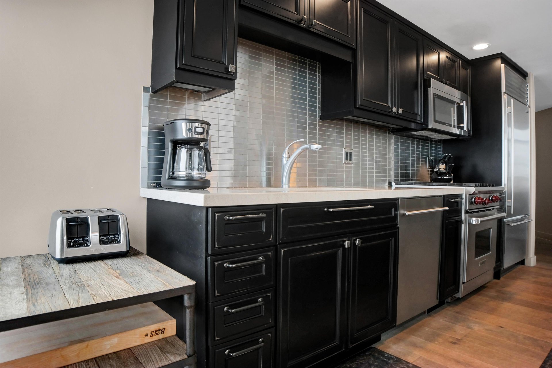 Modern kitchen with dark wood cabinetry, stone countertops, tile backsplash, coffee maker and stainless steel dishwasher.