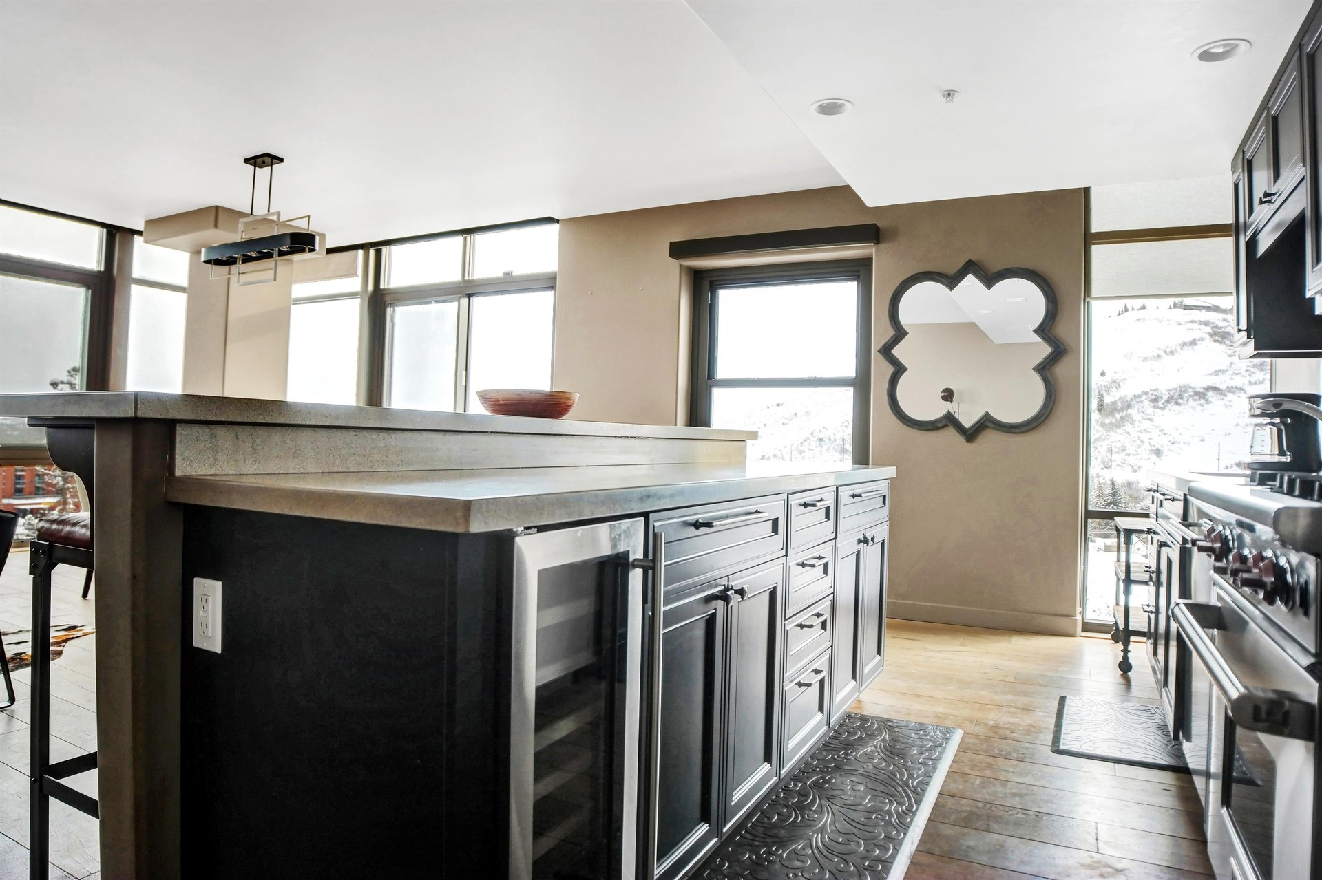 Spacious kitchen island with dark wood cabinetry, stone countertop, beverage cooler and open living area beyond.